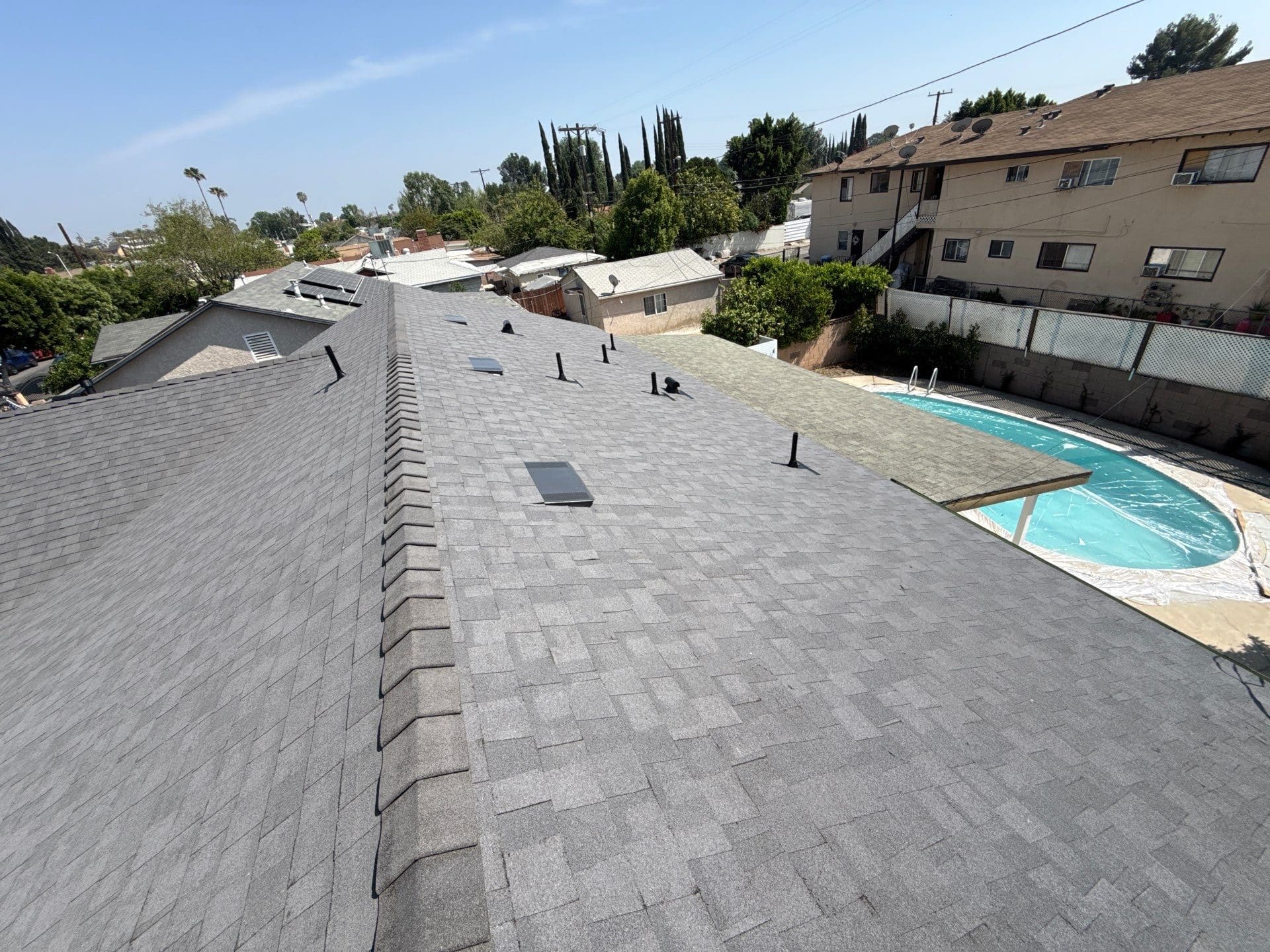 Gray asphalt shingle roof with ridge, skylights, pipe boots, pool visible — Roof Replacement Inc