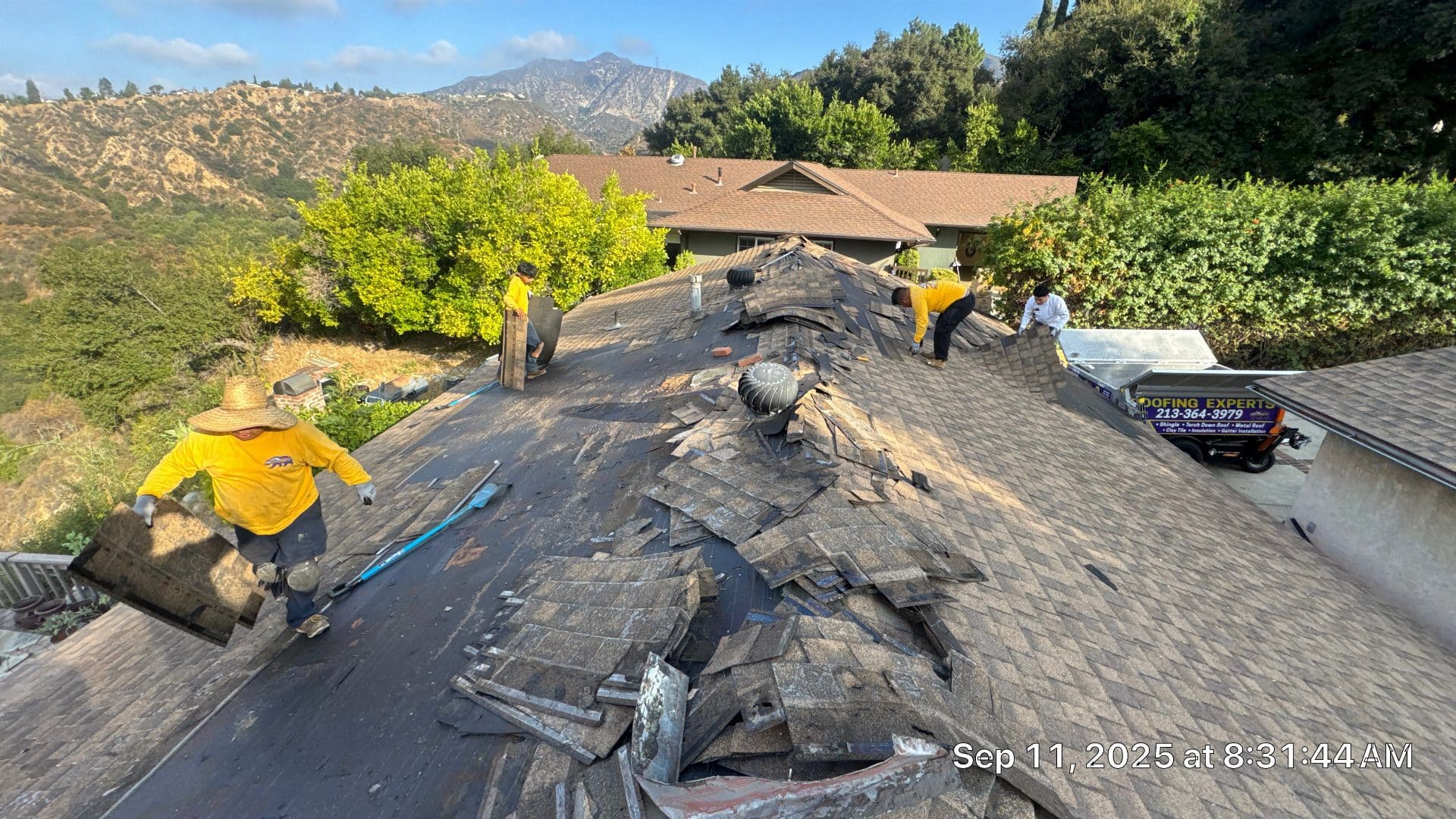 Crew removing worn asphalt shingles from steep residential roof in Altadena | Roof Replacement Inc crew removing worn asphalt shingles from steep residential roof — Altadena — Roof Replacement Inc