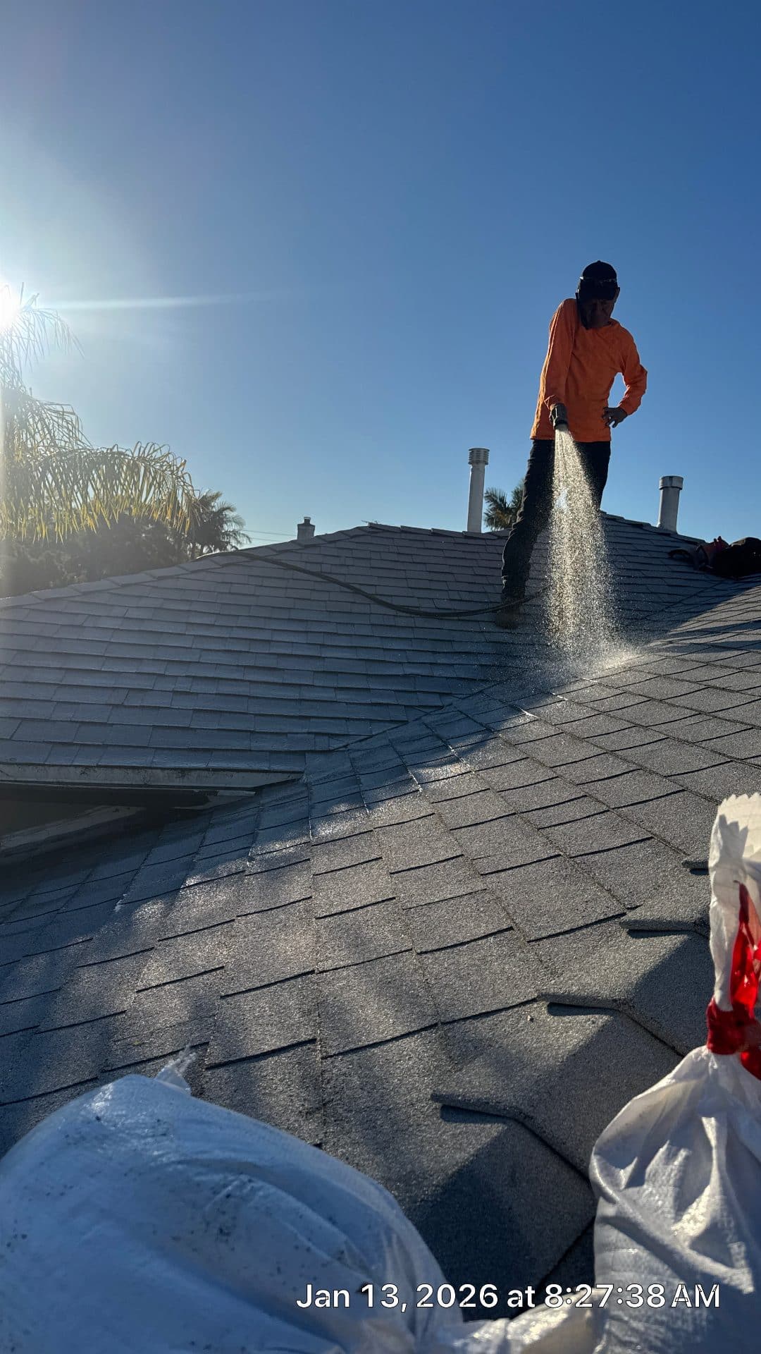 Worker in silhouette spraying treatment on asphalt shingle roof ridge | Roof Replacement Inc Worker in silhouette spraying treatment on asphalt shingle roof ridge — Roof Replacement Inc