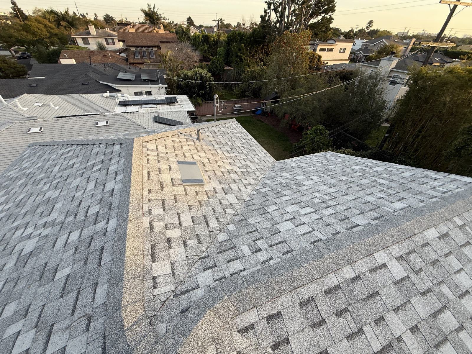 Asphalt shingle roof with valley flashing and roof vent, suburban neighborhood background. — Roof Replacement Inc