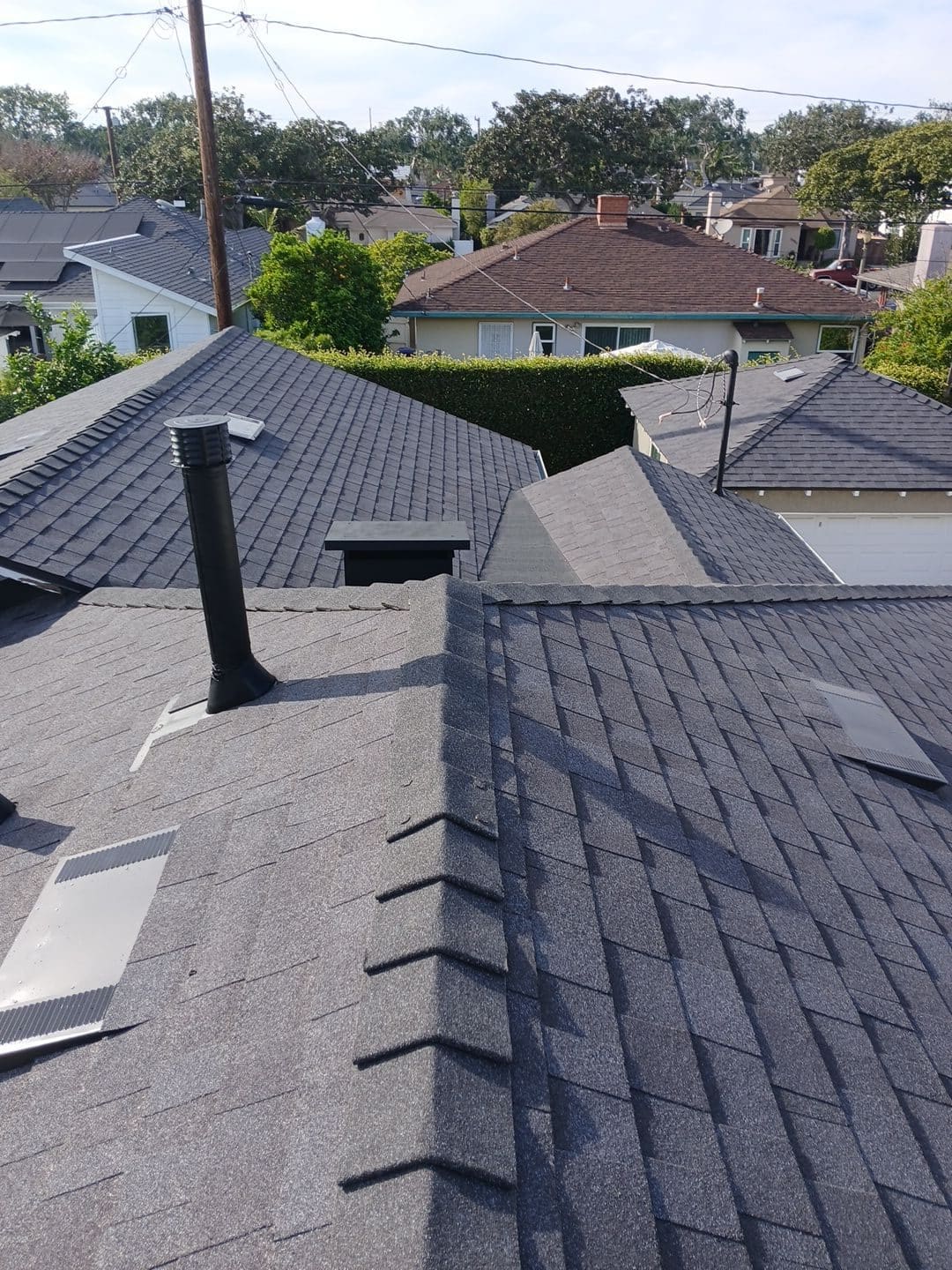 Dark gray asphalt shingle roof with vent pipe and skylight hatch — Roof Replacement Inc