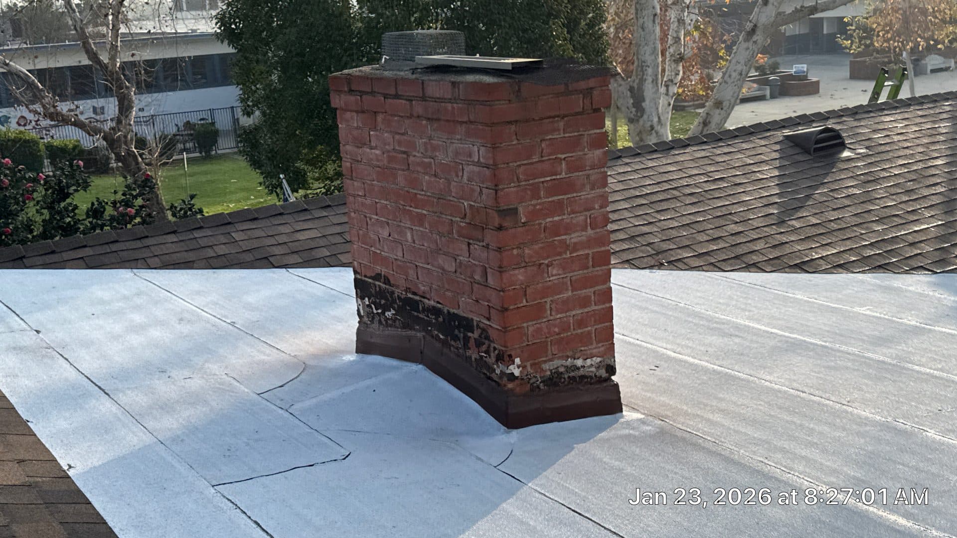 brick chimney on flat white roof with deteriorated base flashing — Burbank — Roof Replacement Inc