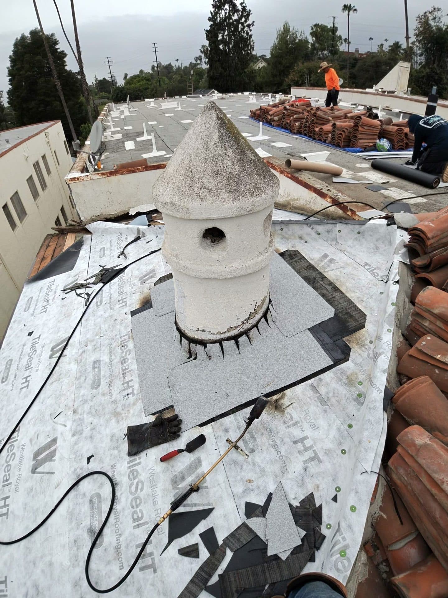 Chimney pot re-flashed with torch-down membrane, clay tiles stacked nearby — Roof Replacement Inc
