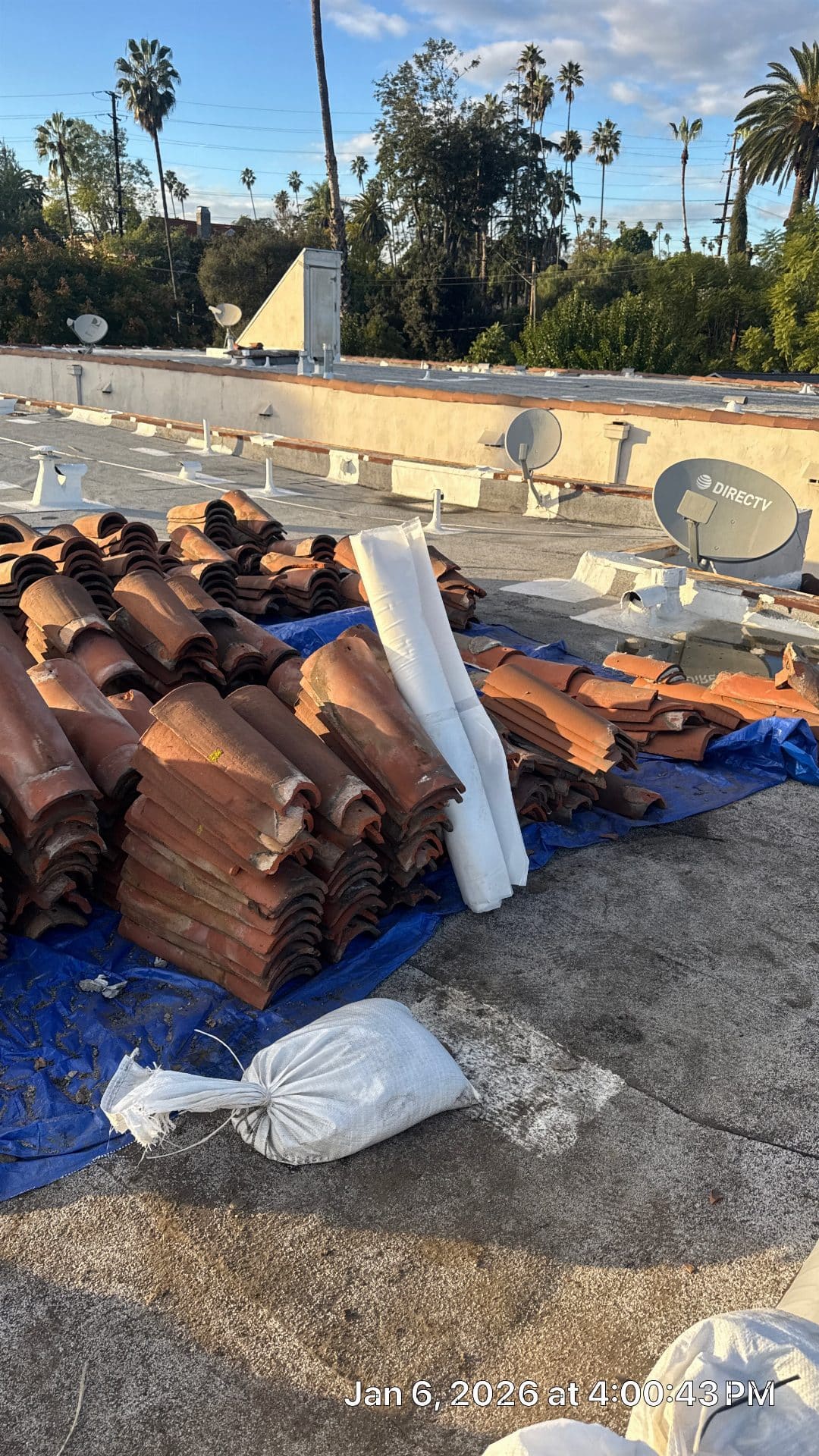 Stacked clay barrel tiles on blue tarp, flat roof, satellite dishes | Roof Replacement Inc Stacked clay barrel tiles on blue tarp, flat roof, satellite dishes — Roof Replacement Inc