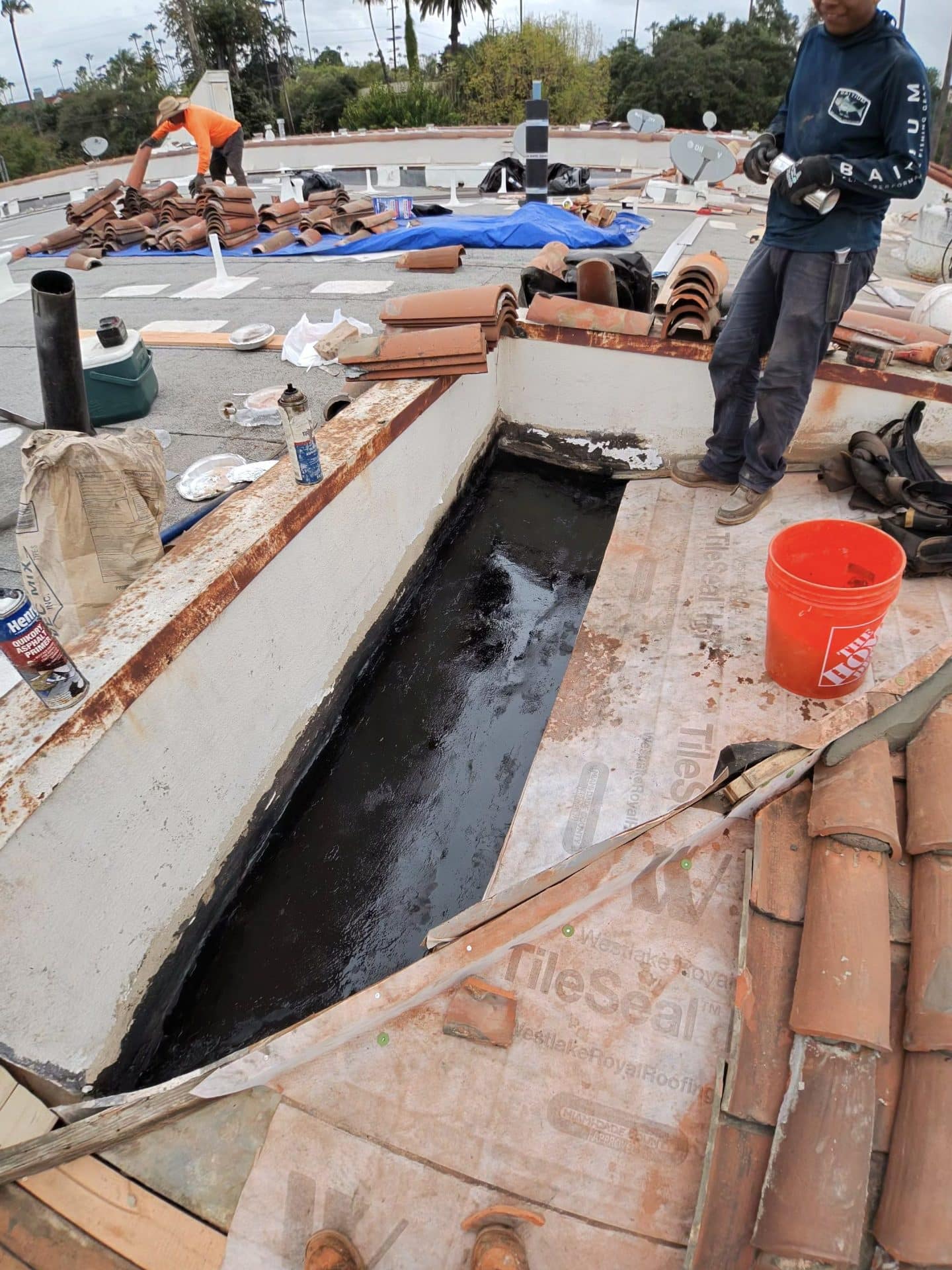 Roof valley with hot tar, clay tiles removed, underlayment and orange bucket visible — Roof Replacement Inc