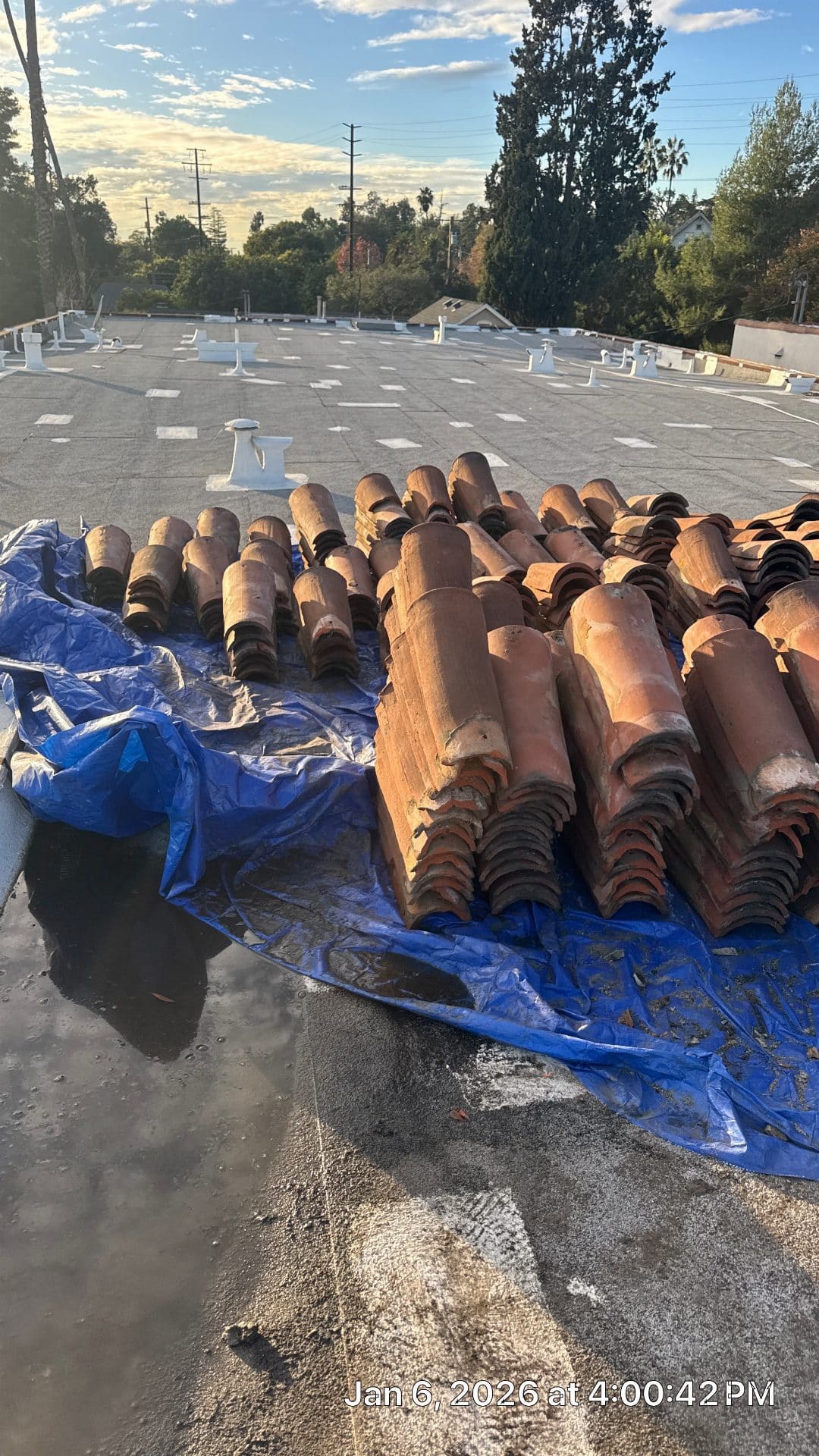 Salvaged clay barrel tiles stacked on flat torch-down roof membrane | Roof Replacement Inc Salvaged clay barrel tiles stacked on flat torch-down roof membrane — Roof Replacement Inc