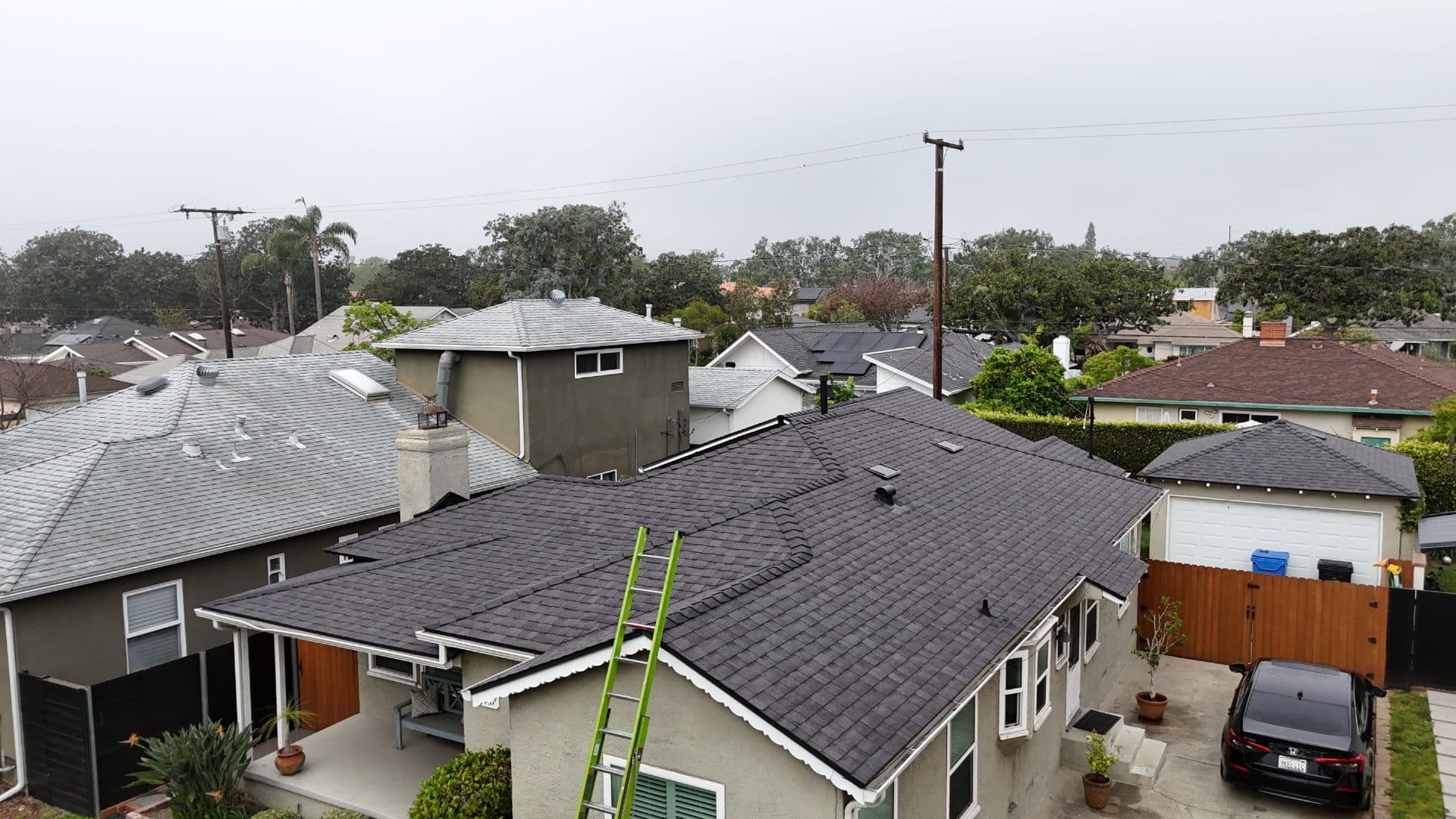 Newly installed dark asphalt shingle roof, green ladder leaning on eave | Roof Replacement Inc Newly installed dark asphalt shingle roof, green ladder leaning on eave — Roof Replacement Inc