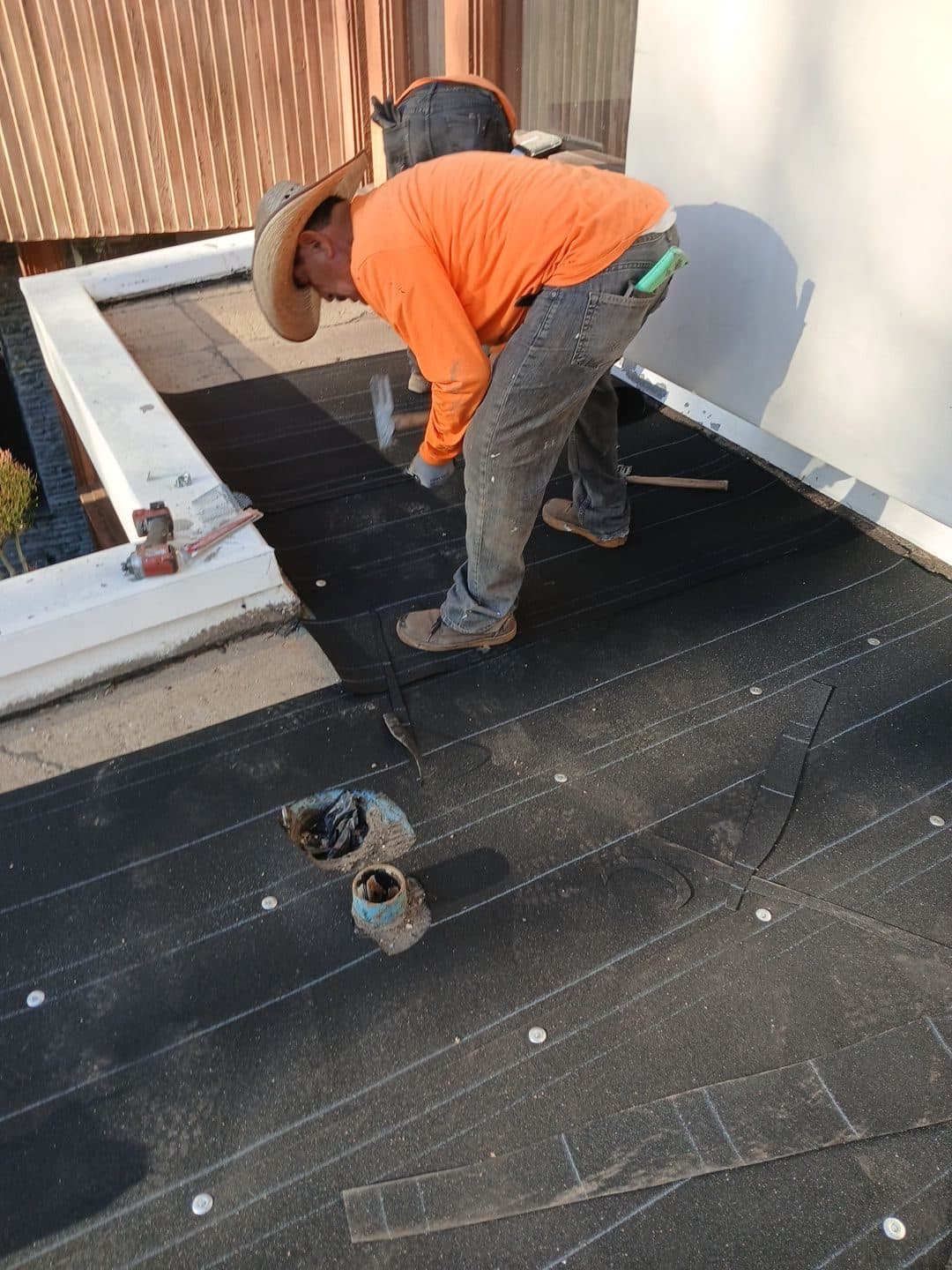 Roofer installing black modified bitumen membrane on flat roof in Beverly Hills | Roof Replacement Inc roofer installing black modified bitumen membrane on flat roof — Beverly Hills — Roof Replacement Inc