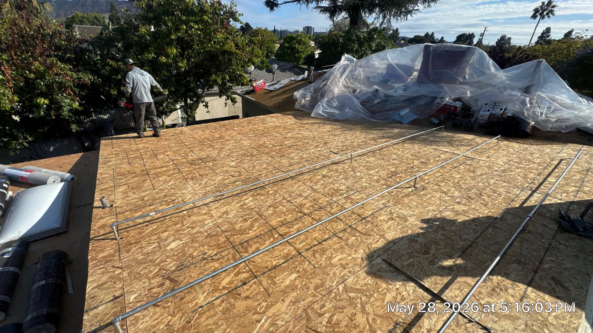 Worker on flat roof with new OSB sheathing decking and conduit rails | Roof Replacement Inc Worker on flat roof with new OSB sheathing decking and conduit rails — Roof Replacement Inc
