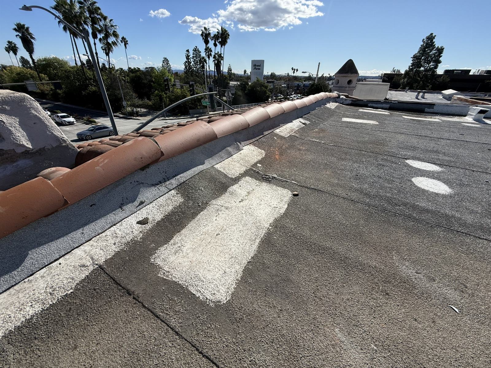 Flat built-up roof with white patch repairs and clay ridge tiles at parapet edge. | Roof Replacement Inc Flat built-up roof with white patch repairs and clay ridge tiles at parapet edge. — Roof Replacement Inc
