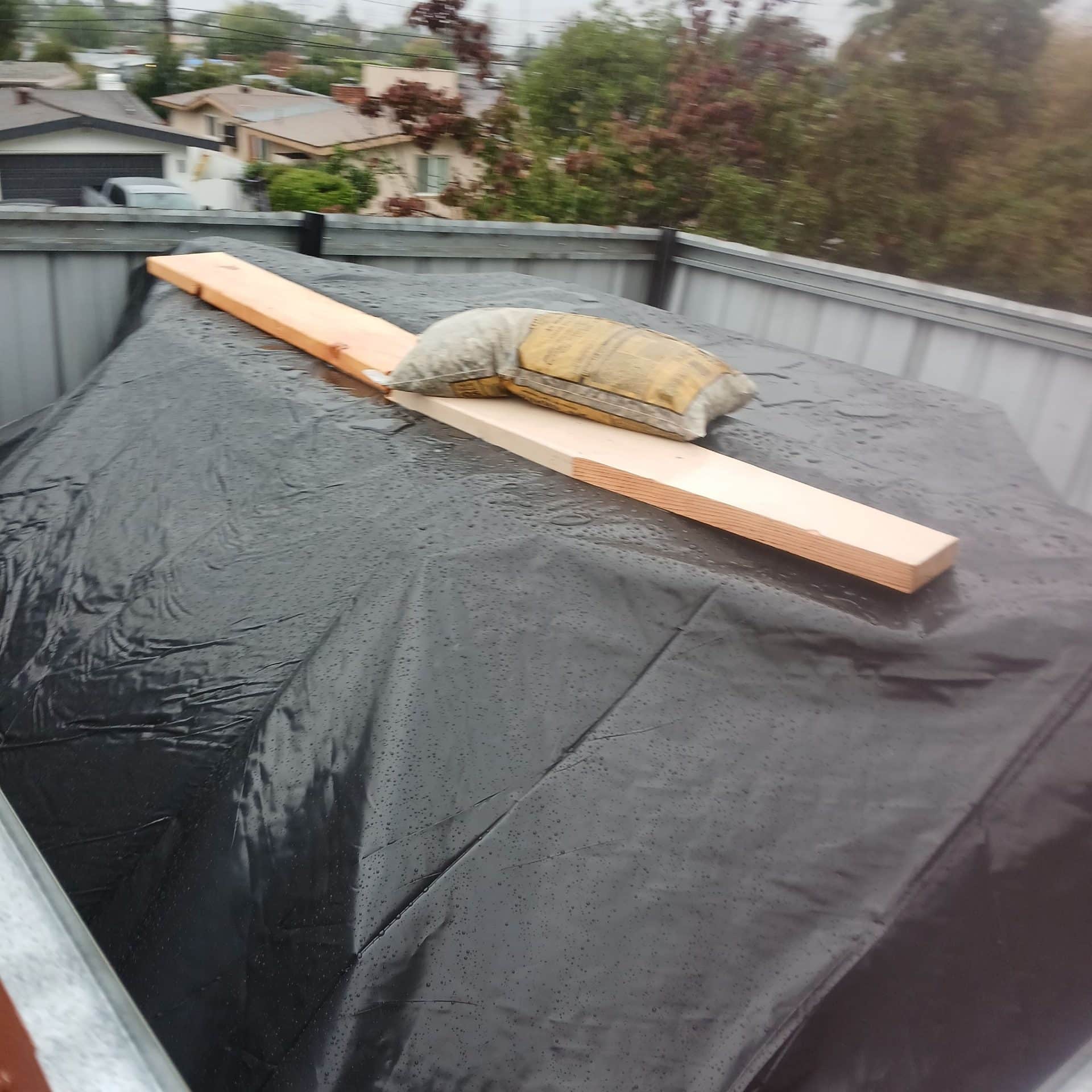 Black poly sheeting over flat roof, lumber board and sandbag weight | Roof Replacement Inc Black poly sheeting over flat roof, lumber board and sandbag weight — Roof Replacement Inc