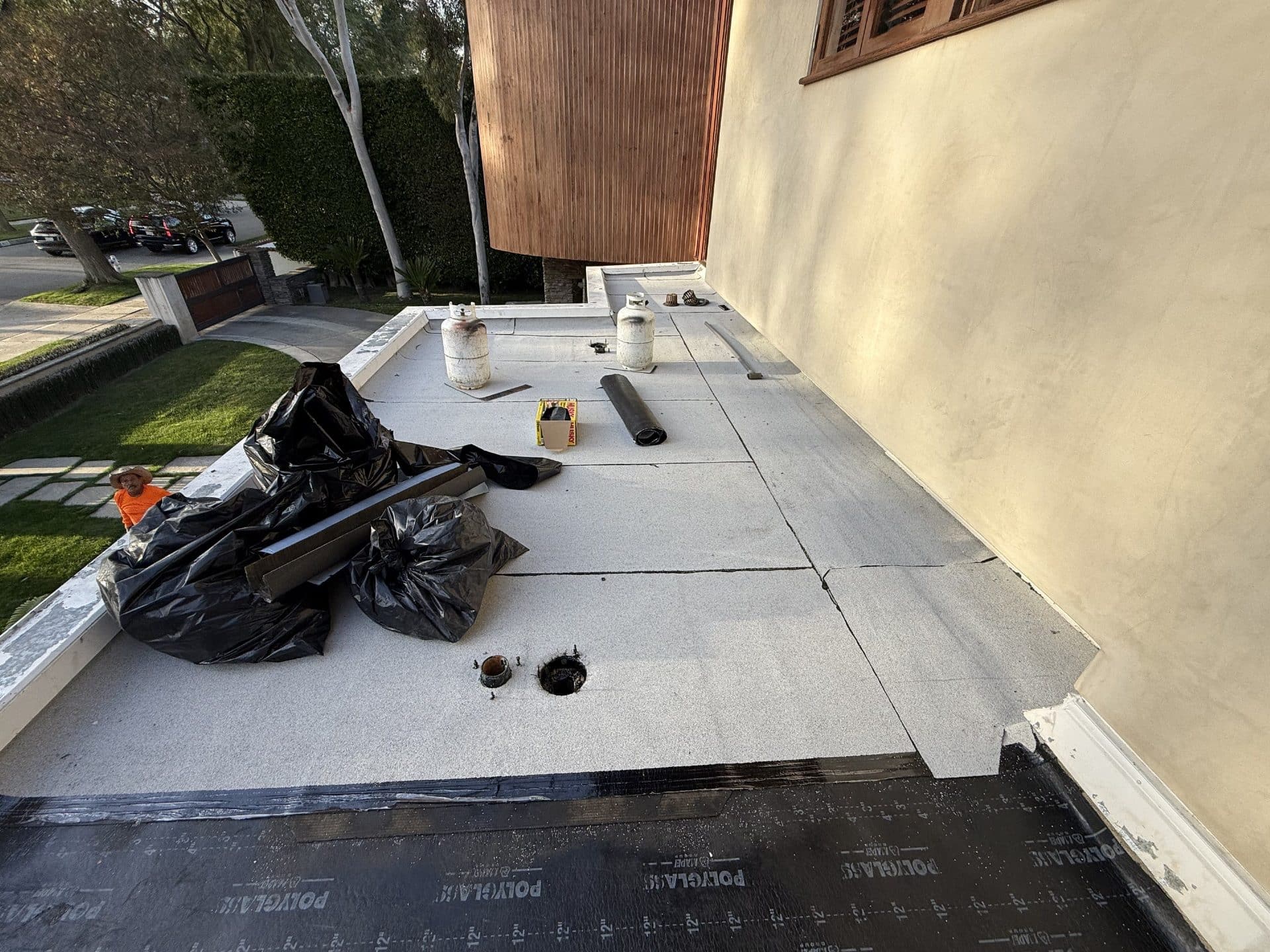 Flat roof installation with polyglás underlayment, propane tanks, and worker in Beverly Hills | Roof Replacement Inc flat roof installation with polyglás underlayment, propane tanks, and worker — Beverly Hills — Roof Replacement Inc