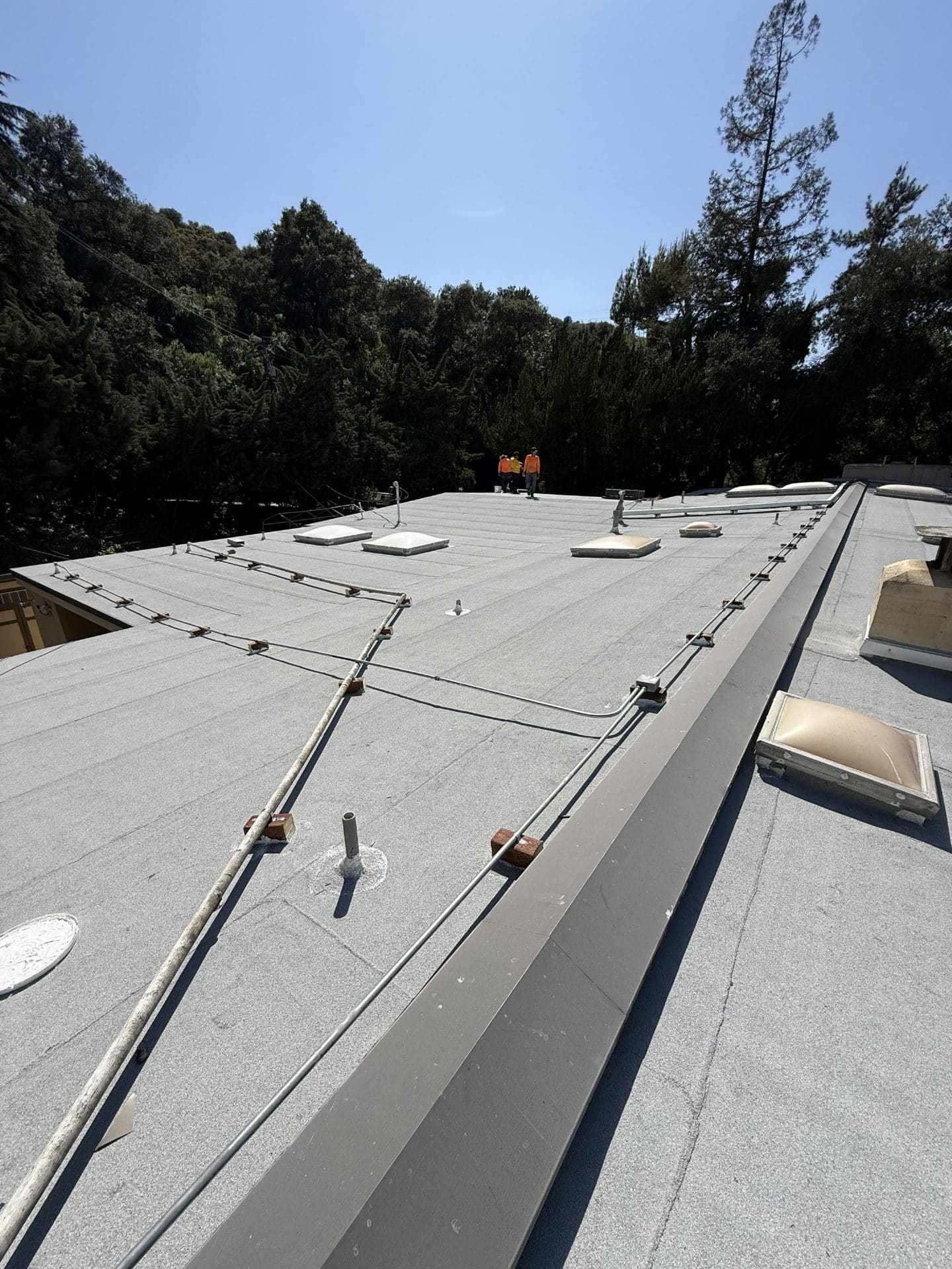 Workers inspecting flat built-up roof with skylights and conduit in La Cañada Flintridge | Roof Replacement Inc workers inspecting flat built-up roof with skylights and conduit — La Cañada Flintridge — Roof Replacement Inc