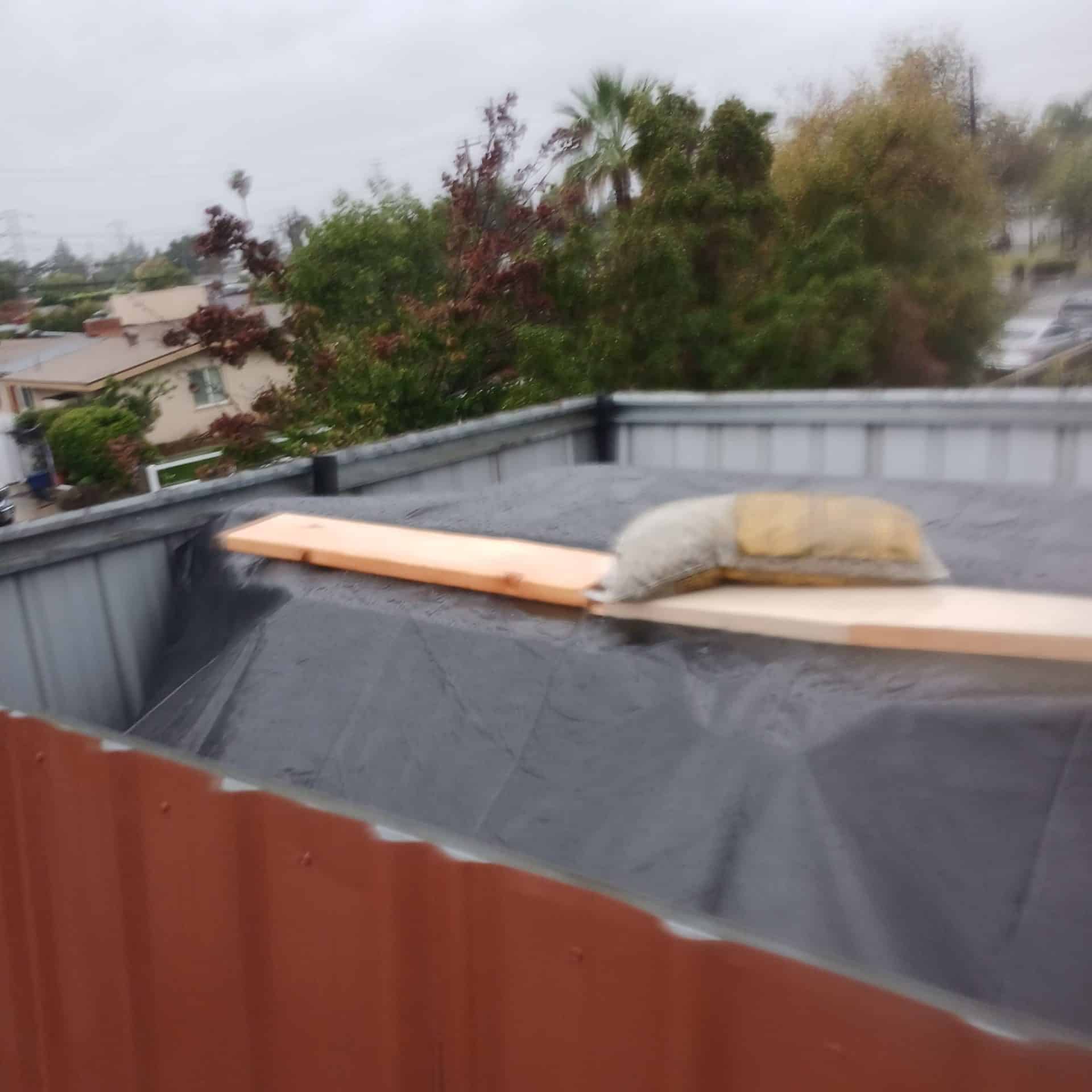 Flat roof covered with black TPO membrane, lumber plank, sandbag weight — Roof Replacement Inc