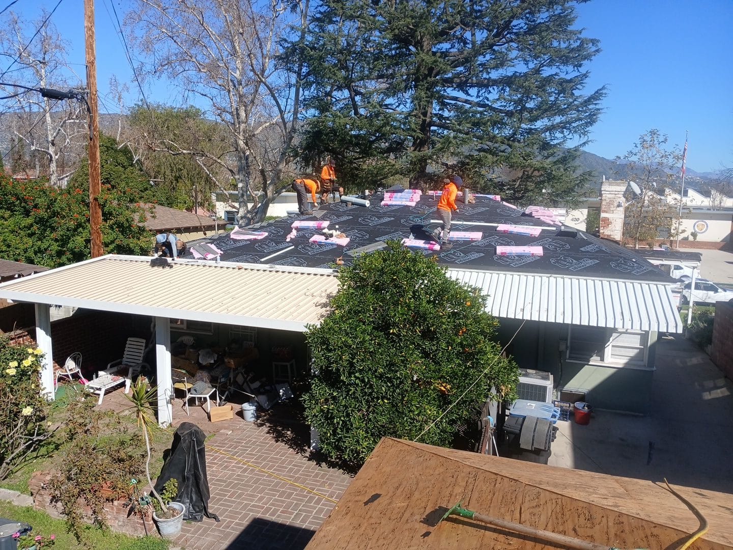 Roofers in orange vests installing underlayment on flat residential roof | Roof Replacement Inc roofers in orange vests installing underlayment on flat residential roof — Roof Replacement Inc