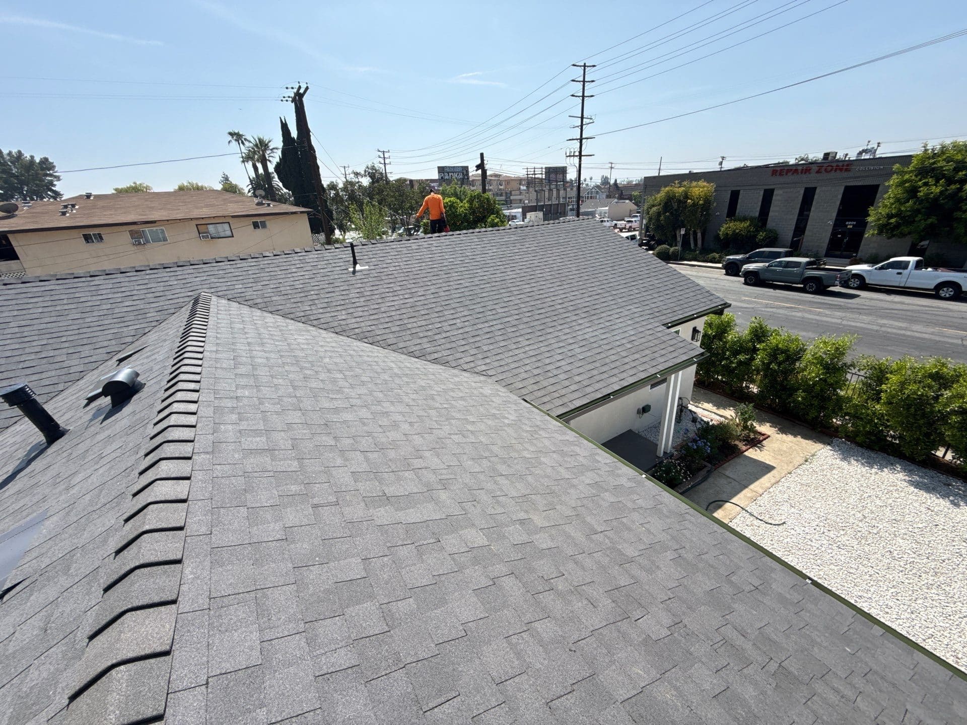 Gray asphalt shingle roof with ridge vents, worker in orange visible on far section — Roof Replacement Inc