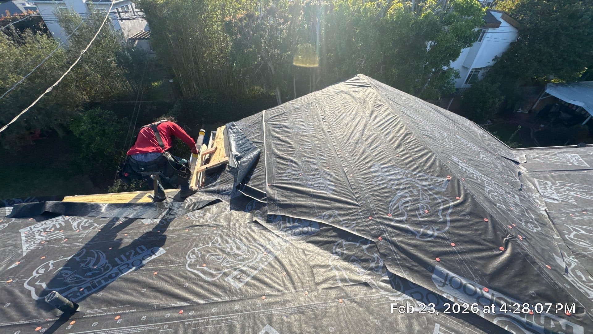 Roofer installs underlayment on hip roof decking, wood framing visible | Roof Replacement Inc Roofer installs underlayment on hip roof decking, wood framing visible — Roof Replacement Inc