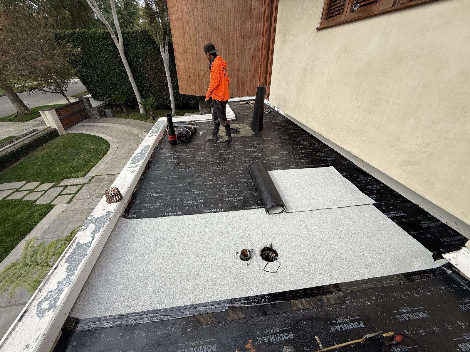 Roofer installing Polyglass modified bitumen rolls on flat roof in Beverly Hills | Roof Replacement Inc roofer installing Polyglass modified bitumen rolls on flat roof — Beverly Hills — Roof Replacement Inc