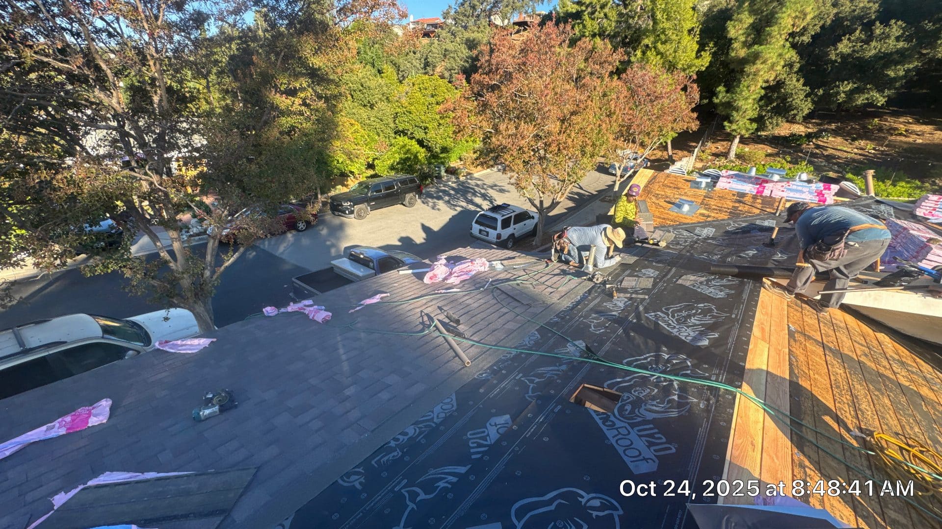 Workers installing underlayment on wood deck roof, shingles stacked nearby | Roof Replacement Inc Workers installing underlayment on wood deck roof, shingles stacked nearby — Roof Replacement Inc