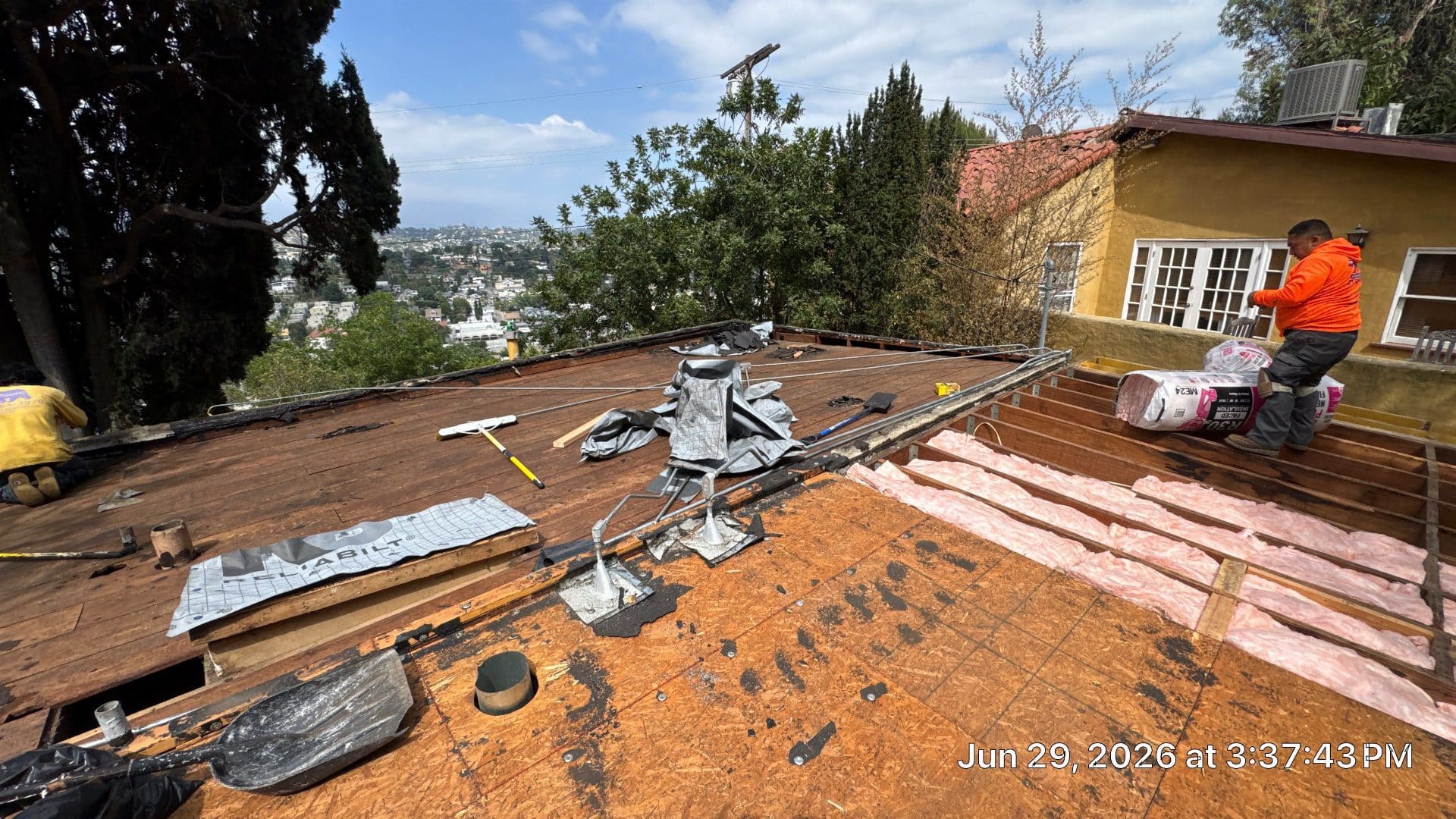 Worker installs fiberglass batt insulation on exposed plywood flat roof deck in North Hollywood | Roof Replacement Inc worker installs fiberglass batt insulation on exposed plywood flat roof deck — North Hollywood — Roof Replacement Inc