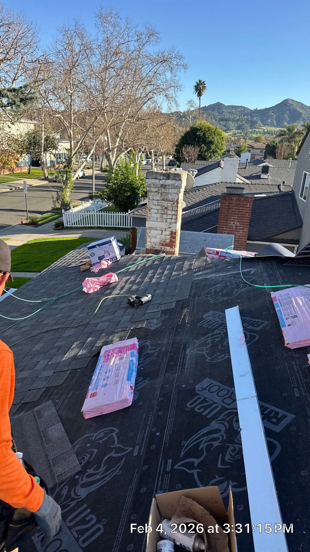 roofer installing underlayment with shingles and two brick chimneys — Roof Replacement Inc