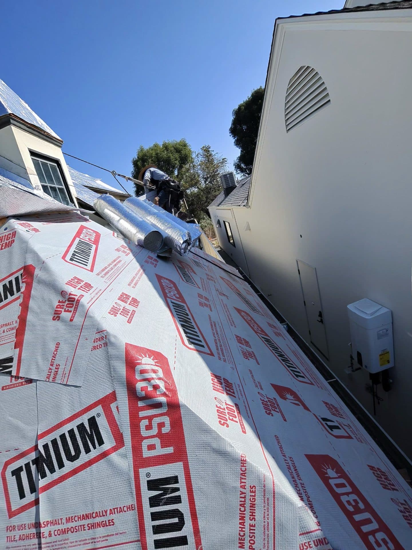 Titanium PSU30 underlayment on steep roof, worker and flex duct visible | Roof Replacement Inc Titanium PSU30 underlayment on steep roof, worker and flex duct visible — Roof Replacement Inc