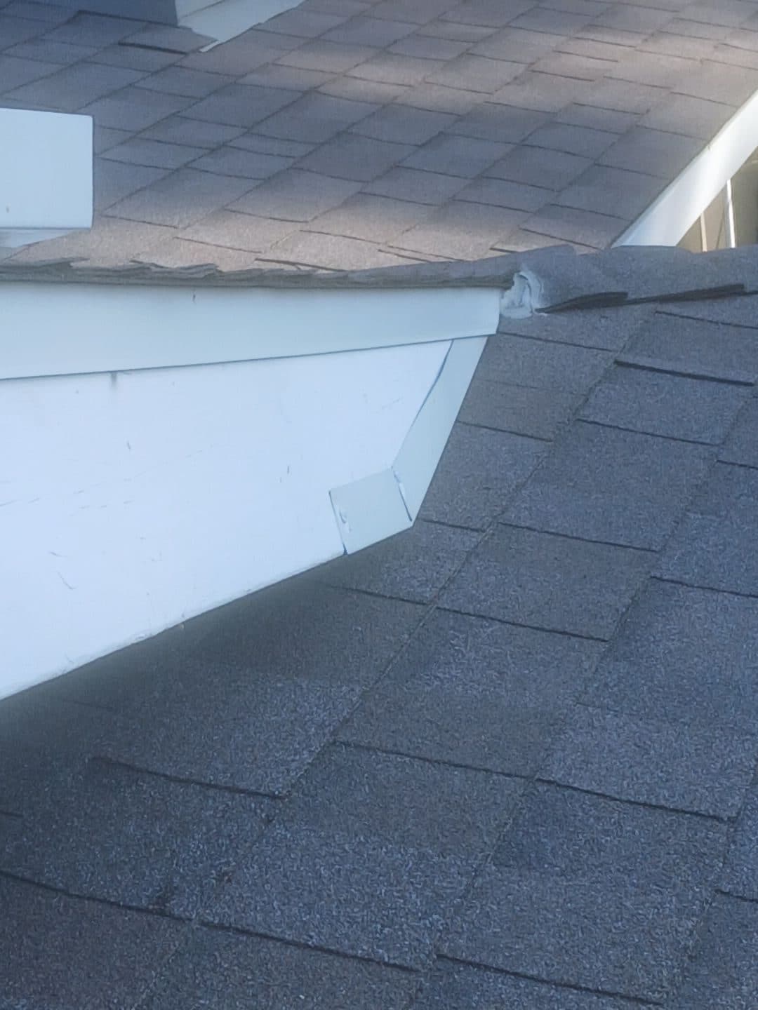 Asphalt shingle roof valley meeting white fascia board, damaged shingles visible | Roof Replacement Inc Asphalt shingle roof valley meeting white fascia board, damaged shingles visible — Roof Replacement Inc