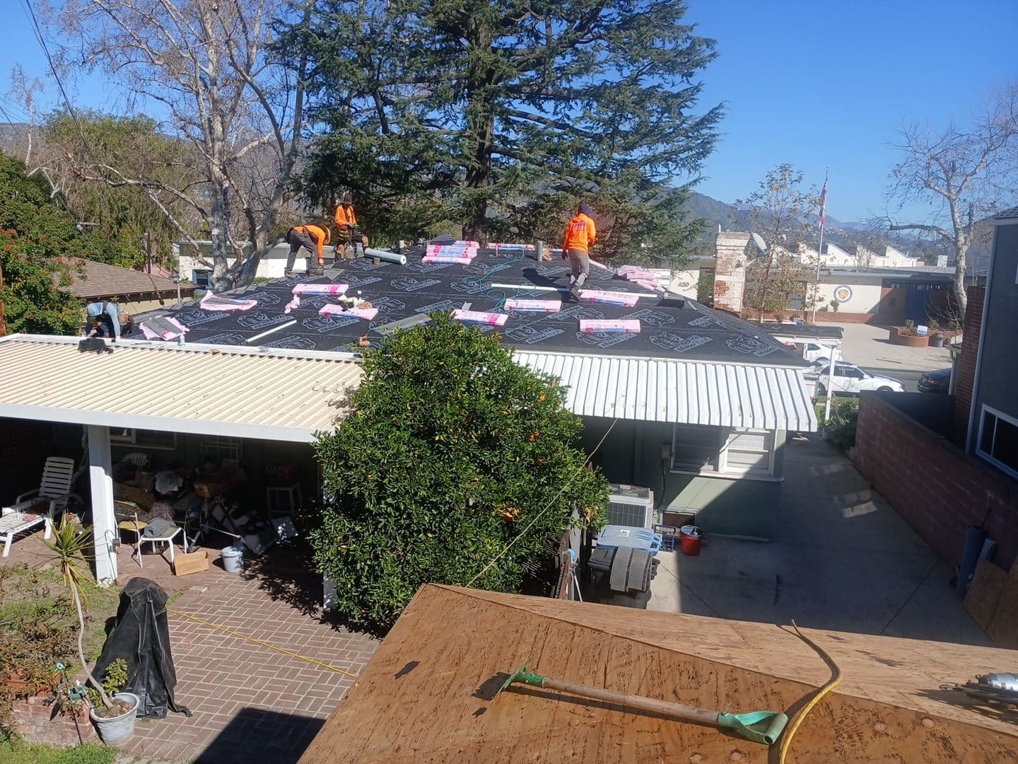 Workers in orange installing roofing underlayment rolls on residential roof | Roof Replacement Inc Workers in orange installing roofing underlayment rolls on residential roof — Roof Replacement Inc