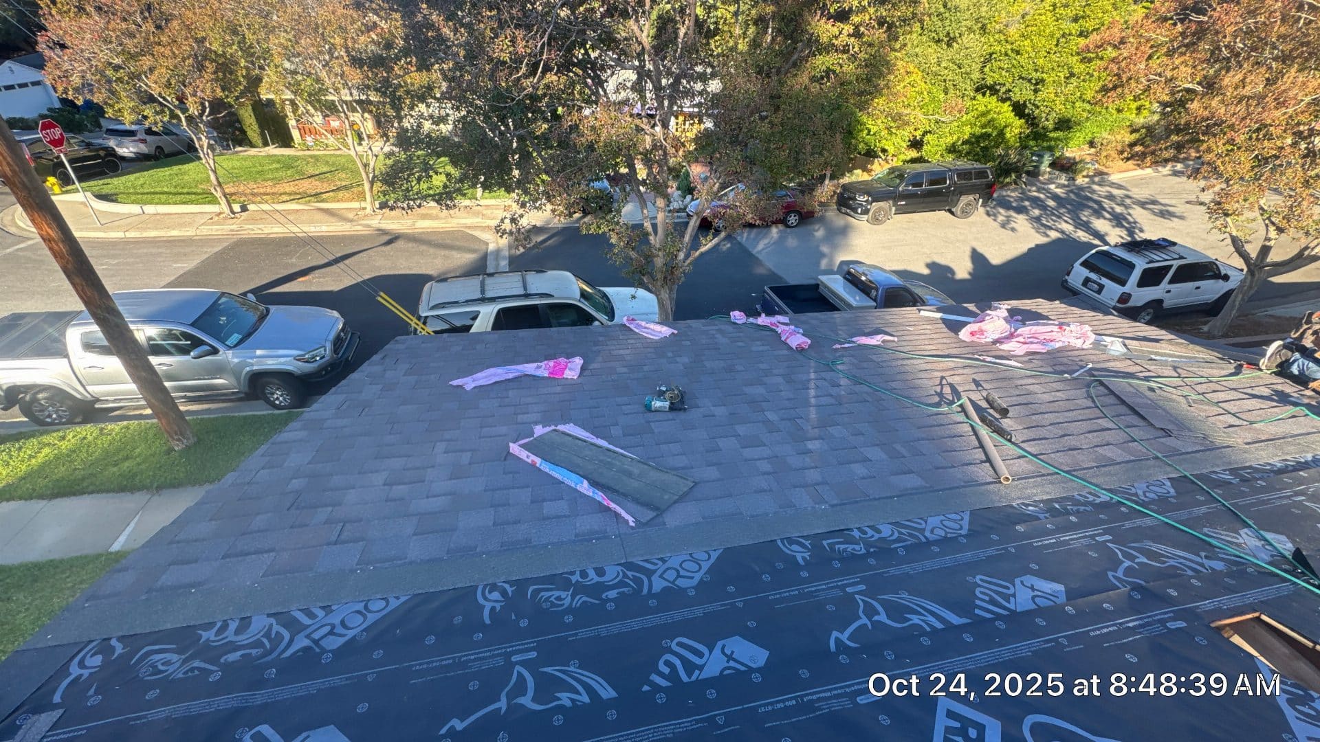 Partial shingle installation over synthetic underlayment, pink insulation scraps on deck — Roof Replacement Inc