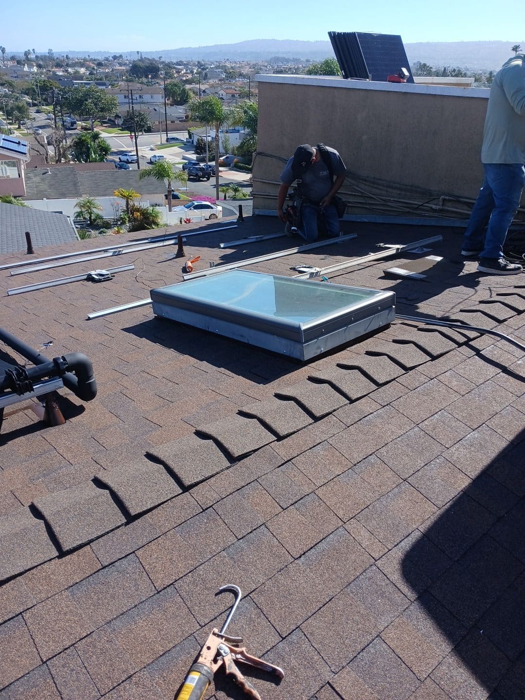 Asphalt shingle roof with skylight, solar rail mounting, caulk gun, workers | Roof Replacement Inc Asphalt shingle roof with skylight, solar rail mounting, caulk gun, workers — Roof Replacement Inc