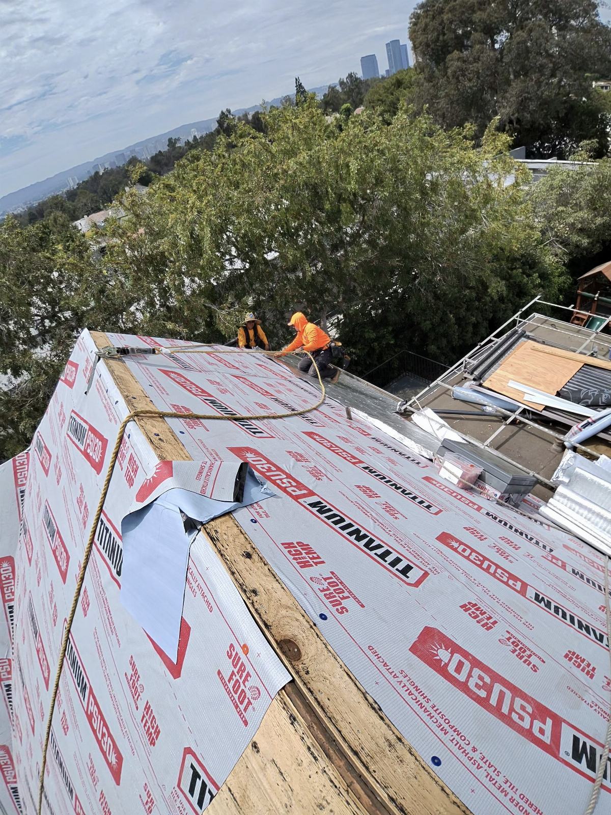 Two workers installing Titanium PSU30 underlayment on steep pitched roof | Roof Replacement Inc Two workers installing Titanium PSU30 underlayment on steep pitched roof — Roof Replacement Inc