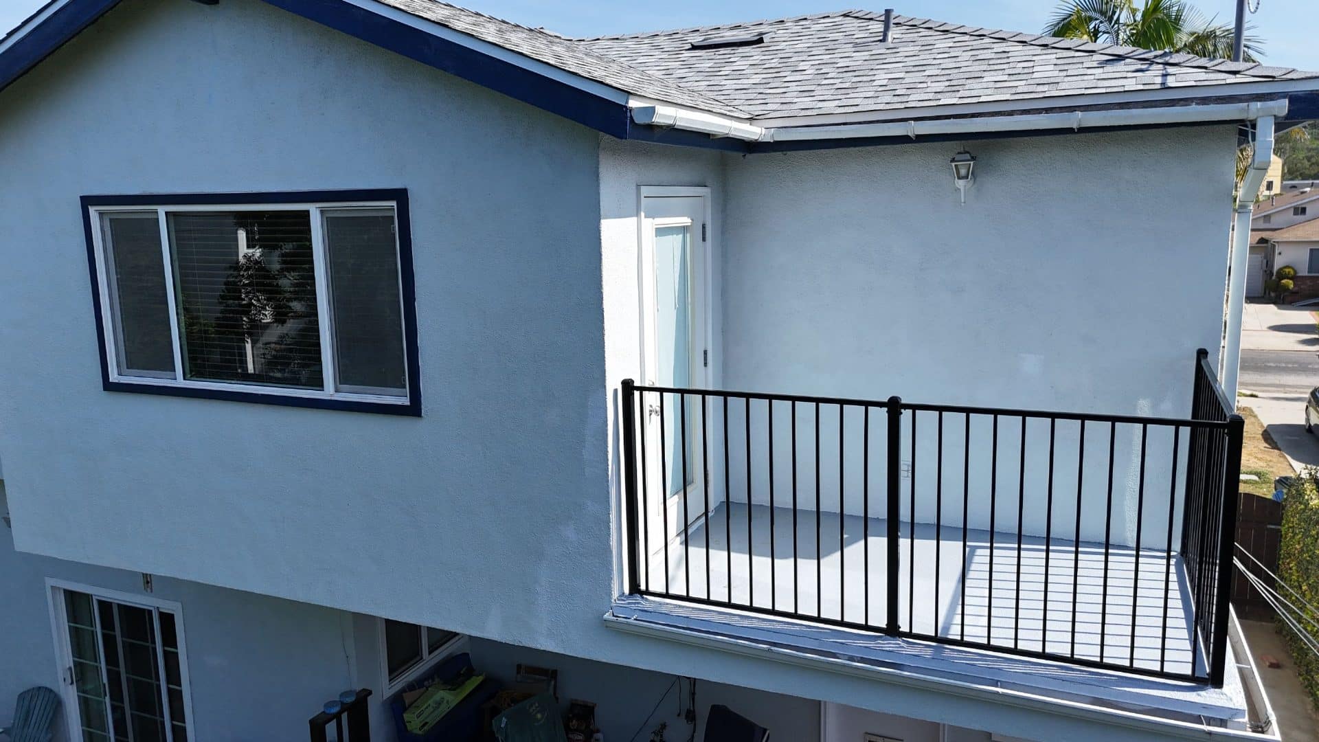 Two-story stucco home with asphalt shingle roof and second-floor deck with black iron railing — Roof Replacement Inc