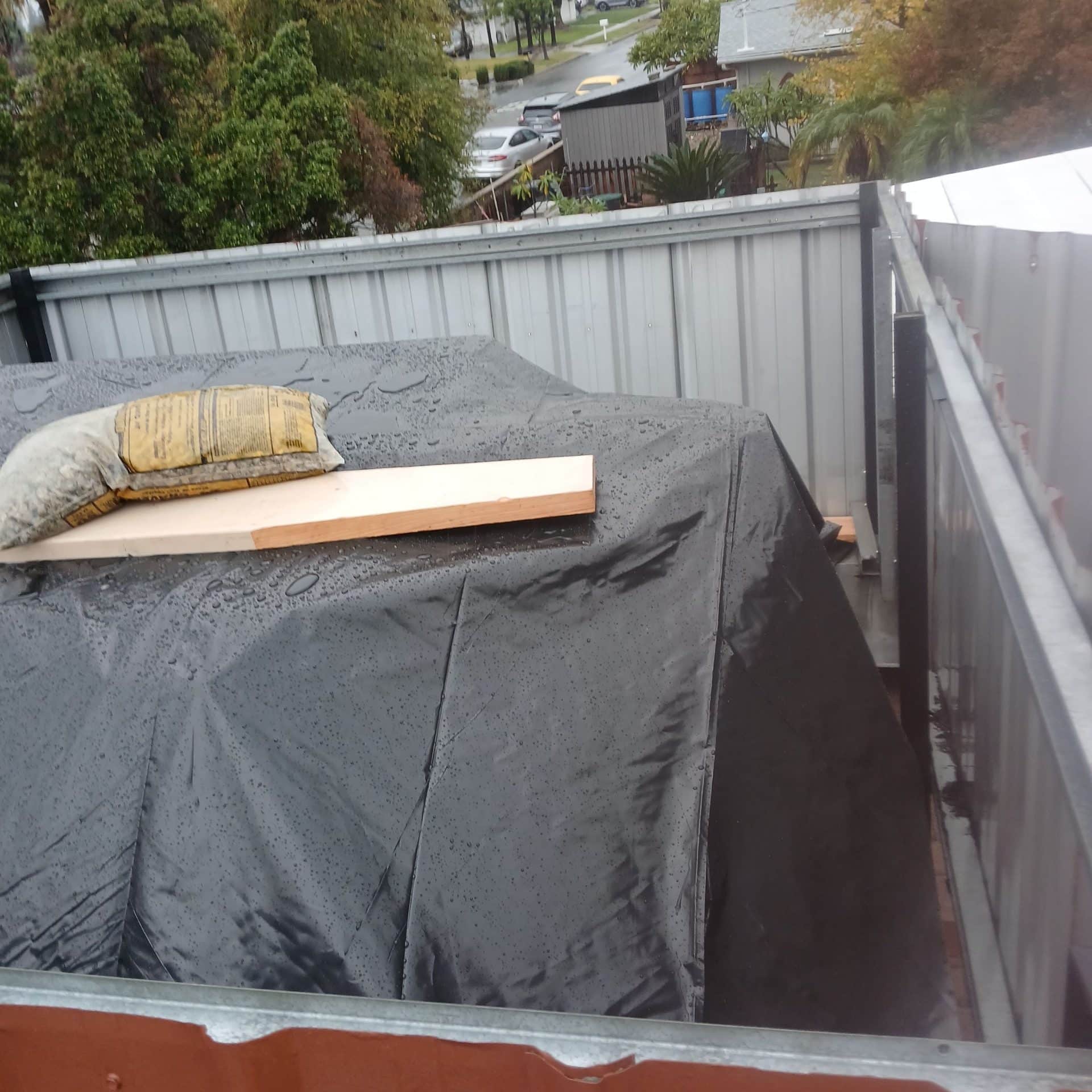 Wet black plastic tarp covering framed roof structure in skip bin — Roof Replacement Inc