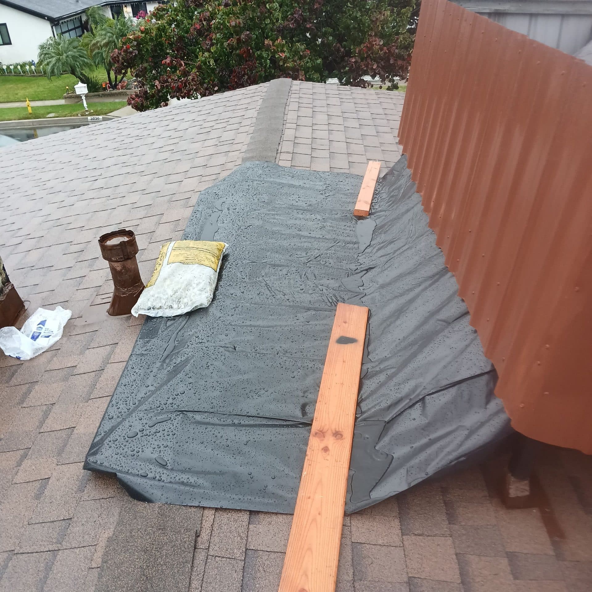 Roof section covered with tarp weighted by lumber boards, wet shingles | Roof Replacement Inc Roof section covered with tarp weighted by lumber boards, wet shingles — Roof Replacement Inc
