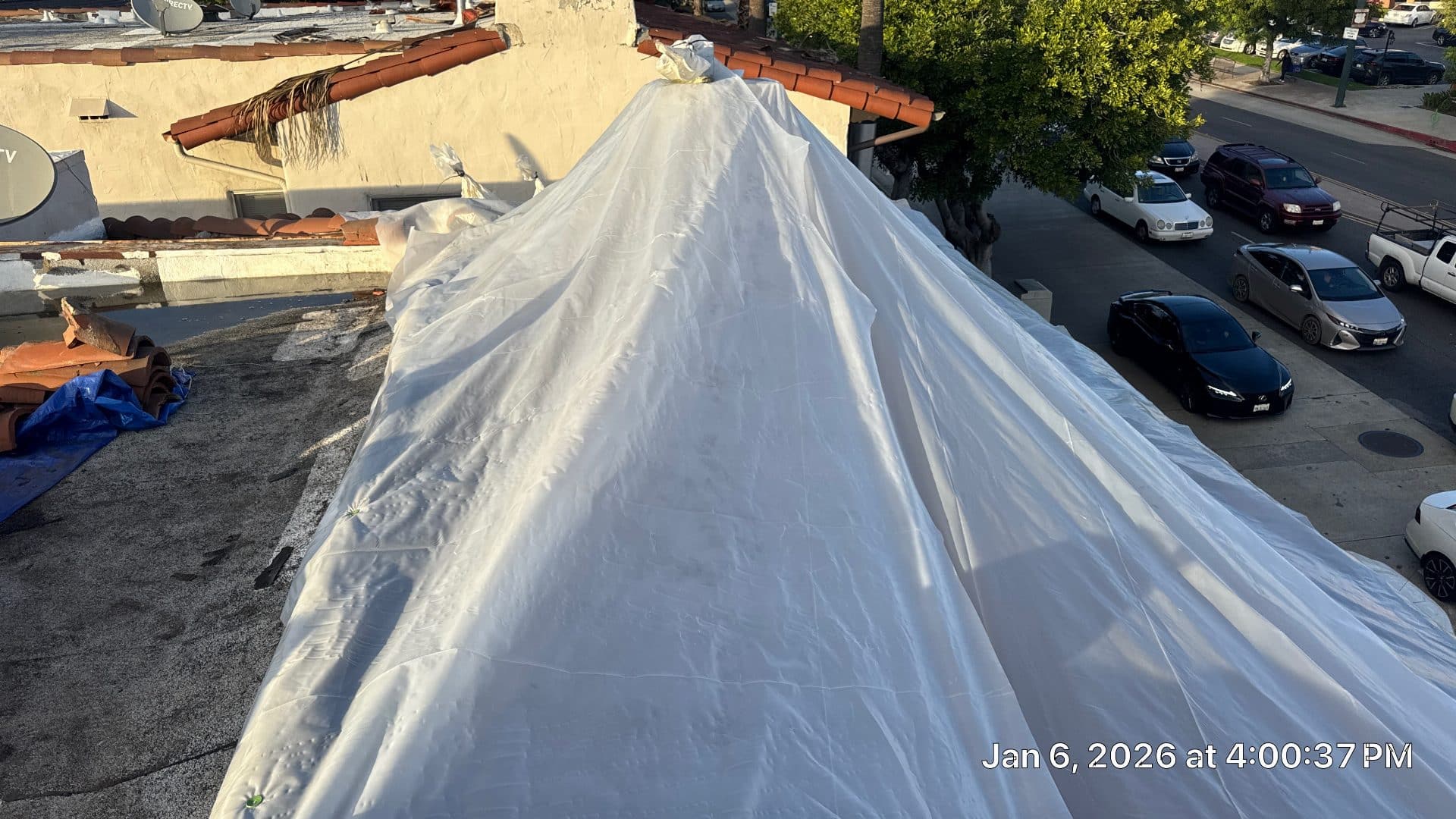 White poly tarp covering pitched tile roof under repair | Roof Replacement Inc White poly tarp covering pitched tile roof under repair — Roof Replacement Inc
