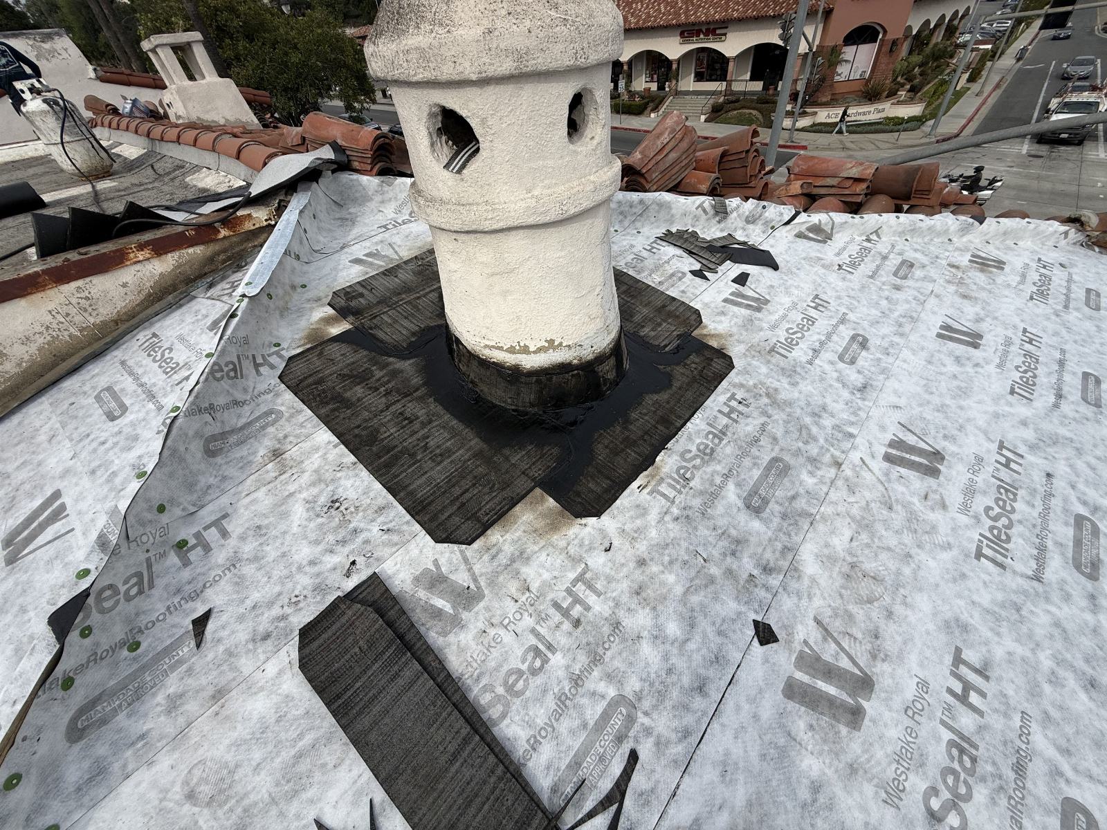 Roof underlayment TileSeal HT installed around decorative chimney tower, clay tiles stacked nearby — Roof Replacement Inc