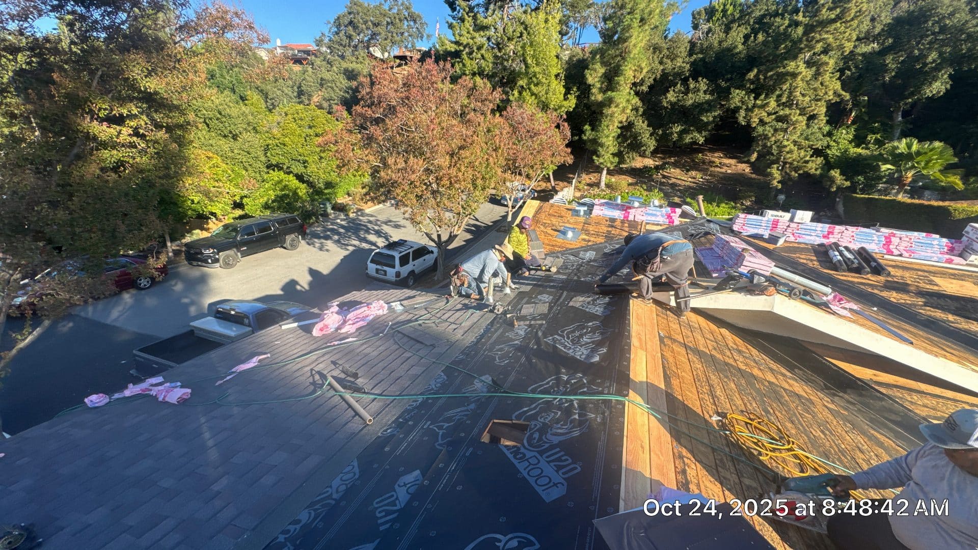 Crew installing synthetic underlayment on wood deck roof, shingle bundles staged — Roof Replacement Inc
