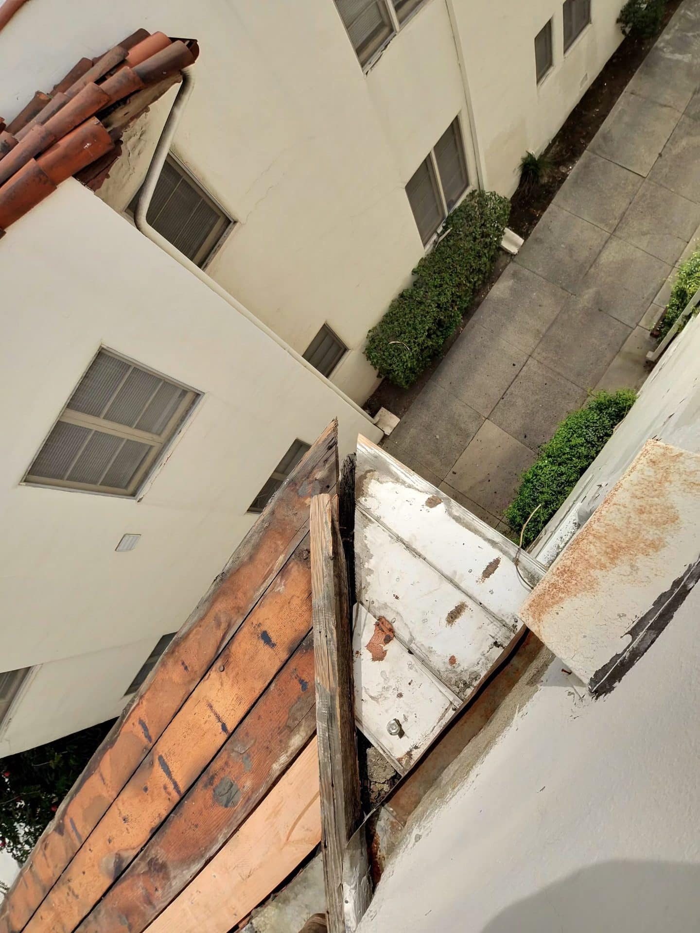 Aged wood fascia, rusted metal flashing, courtyard below multi-story stucco building — Roof Replacement Inc