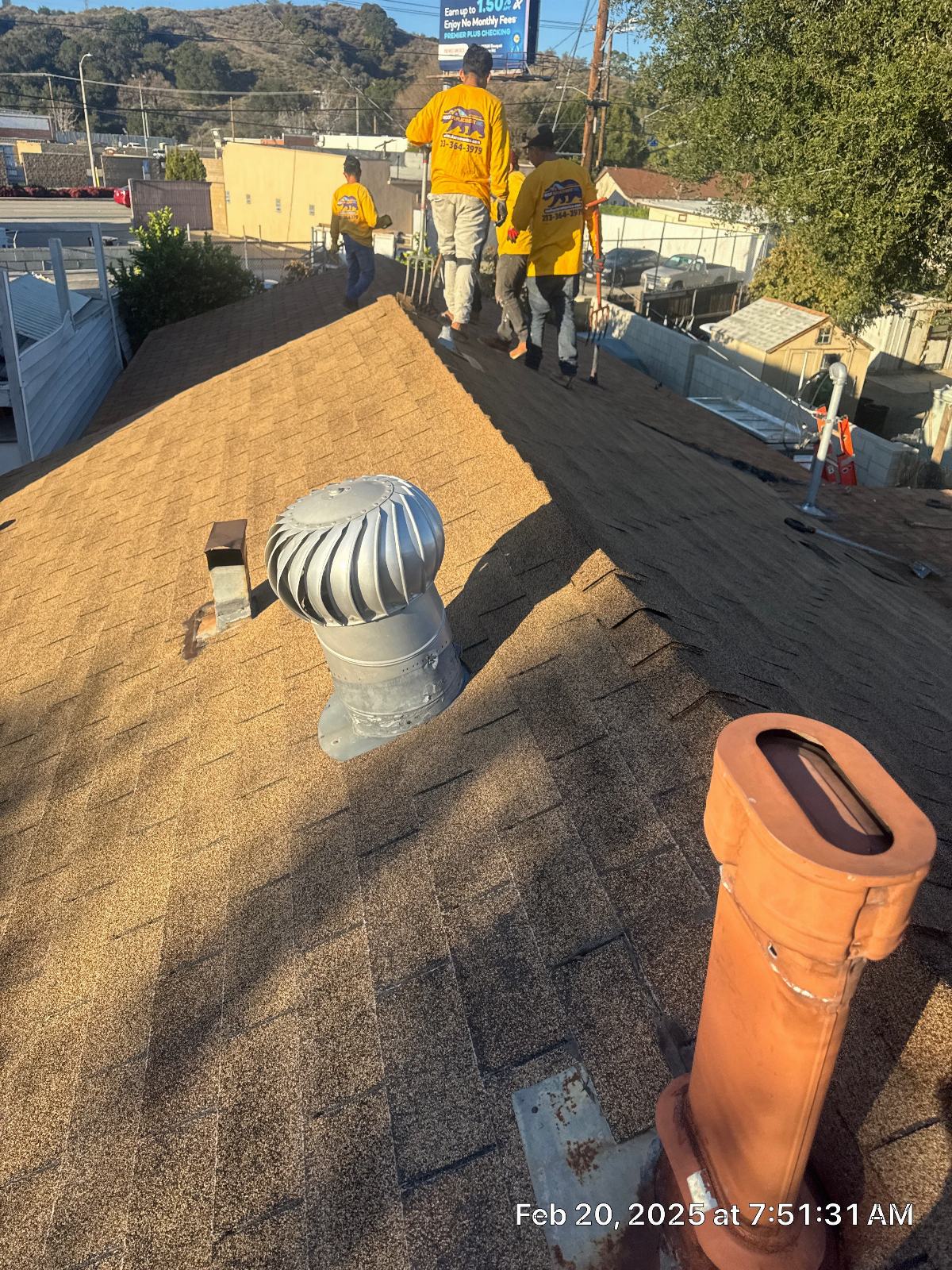 Crew replacing asphalt shingles on pitched roof, turbine vent and clay pipe visible — Roof Replacement Inc
