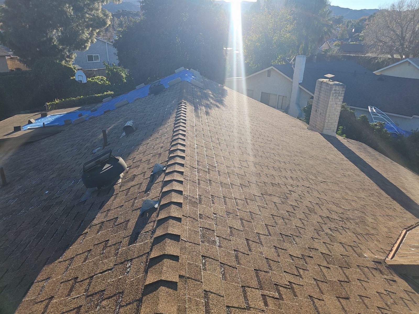 Asphalt shingle roof with ridge cap, vents, chimney, partial blue tarp — Roof Replacement Inc