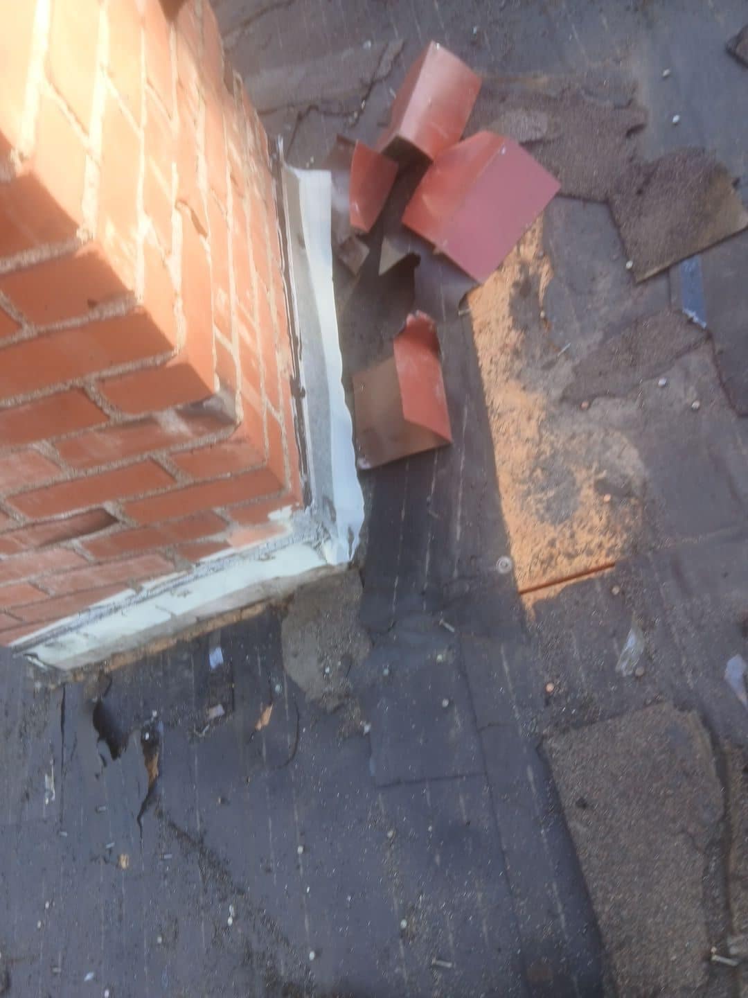 Brick chimney base with deteriorated flashing and loose metal pieces on aged asphalt shingles in Van Nuys | Roof Replacement Inc Brick chimney base with deteriorated flashing and loose metal pieces on aged asphalt shingles — Van Nuys