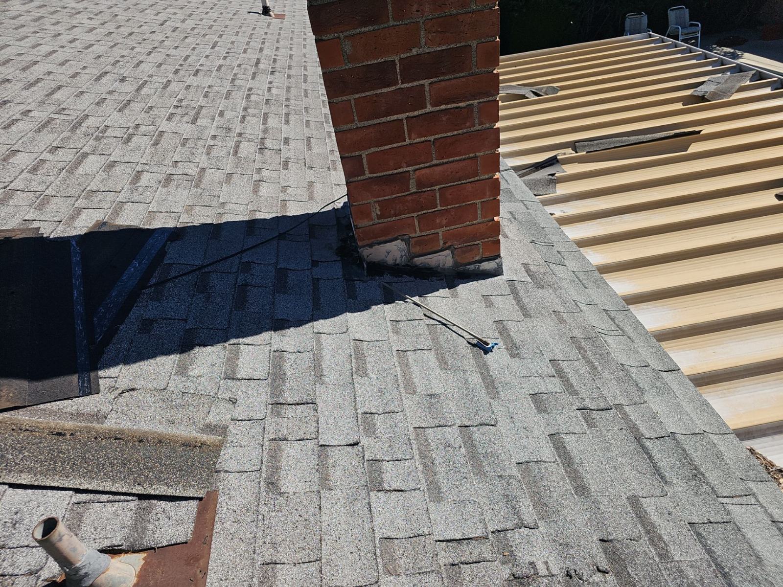 Asphalt shingle roof with brick chimney, missing flashing, exposed underlayment, lumber staging | Roof Replacement Inc Asphalt shingle roof with brick chimney, missing flashing, exposed underlayment, lumber staging — Roof Replacement Inc