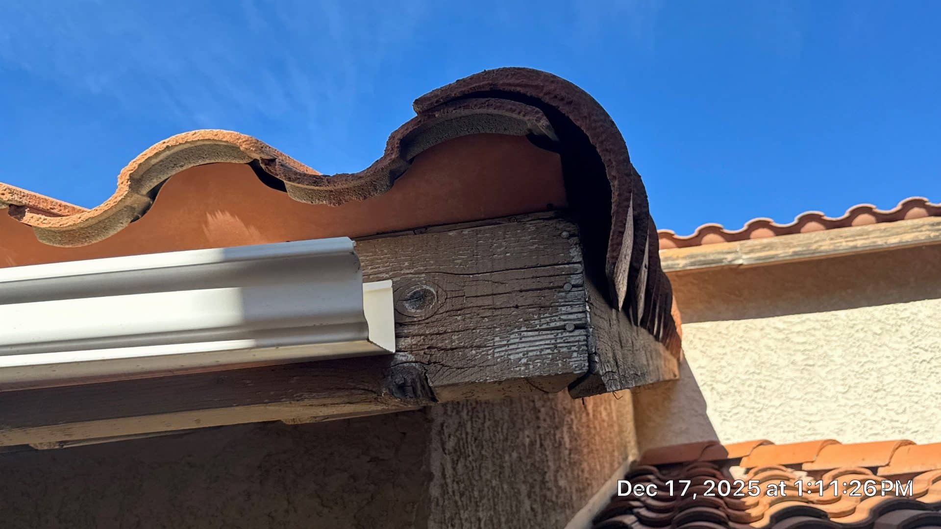Weathered wood fascia board under clay barrel tile roof edge with white gutter | Roof Replacement Inc Weathered wood fascia board under clay barrel tile roof edge with white gutter — Roof Replacement Inc