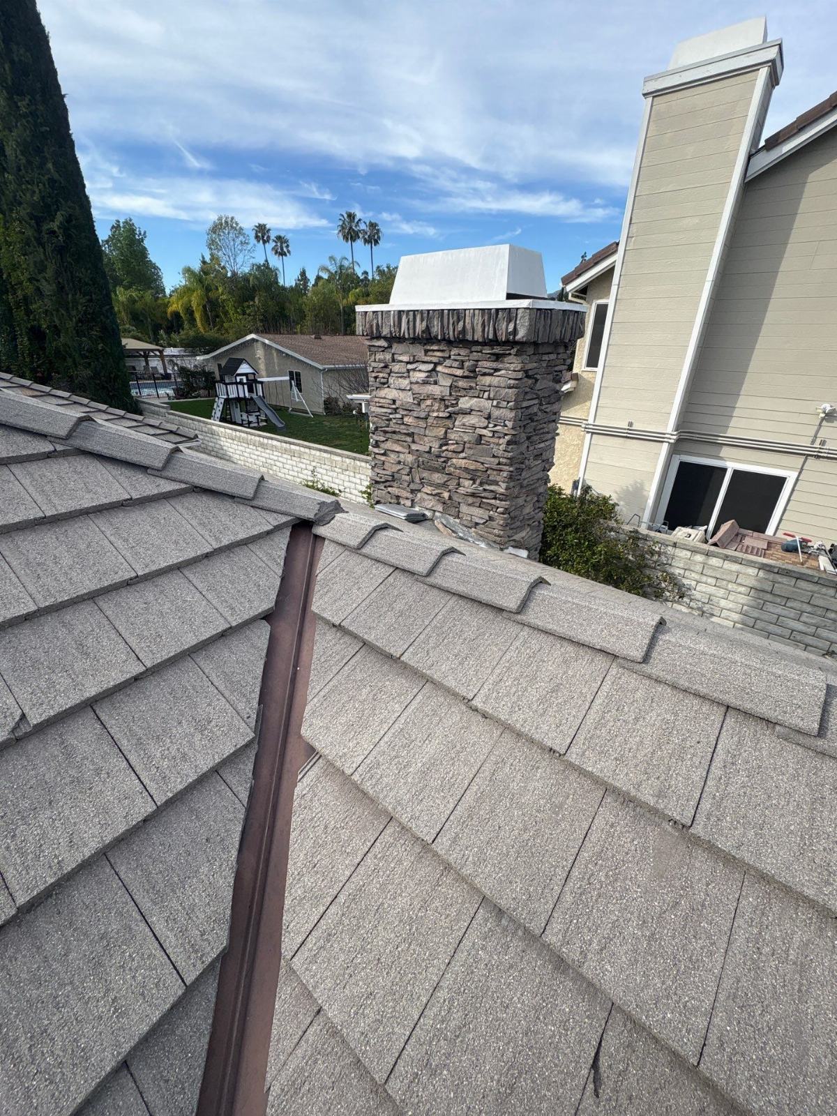 Concrete tile roof with hip ridge, stone chimney, white cap — Northridge — Roof Replacement Inc