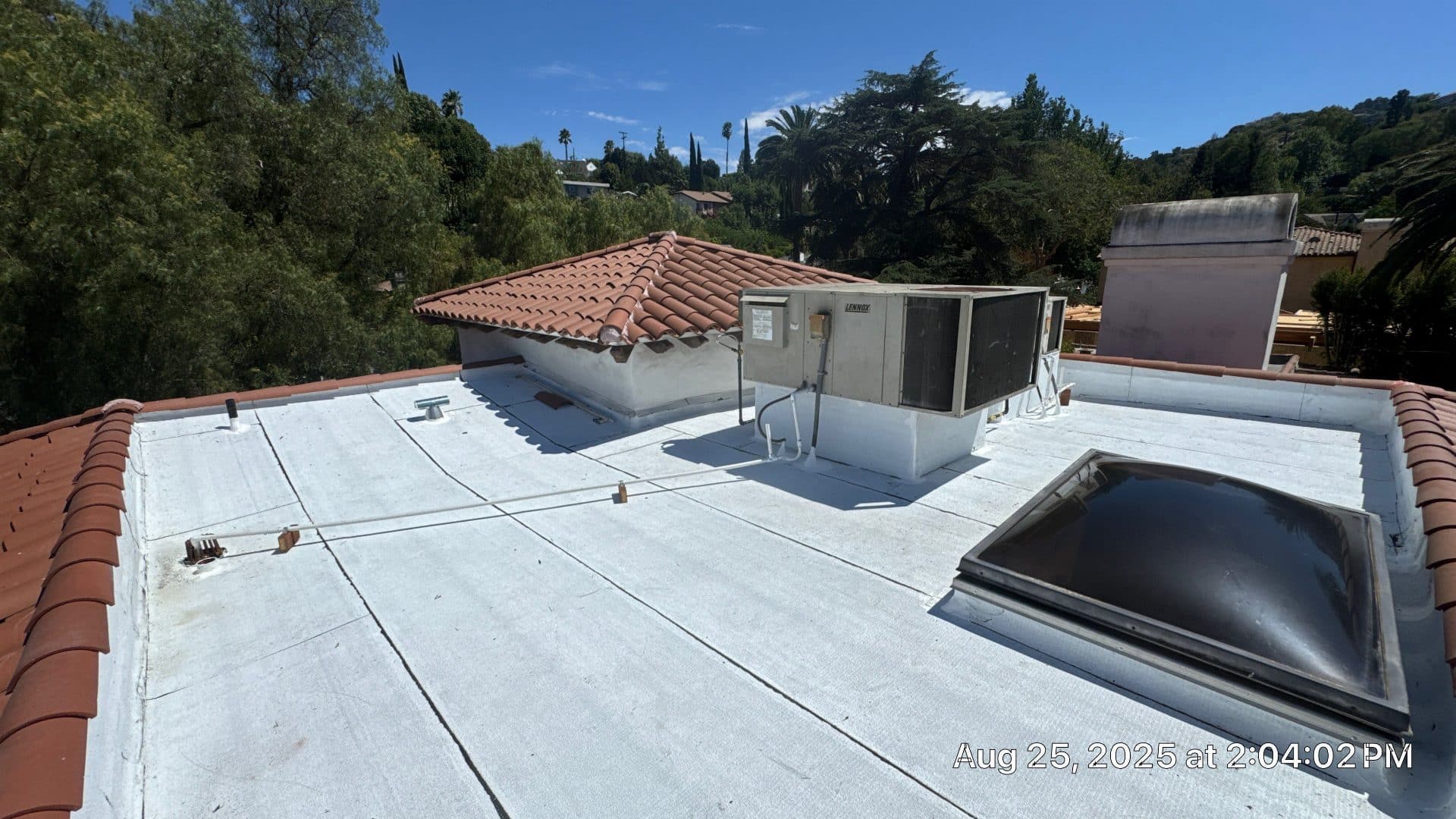 White elastomeric-coated flat roof with a skylight beside a clay tile roof in Sherman Oaks | Roof Replacement Inc White elastomeric-coated flat roof with a skylight beside a clay tile roof — Sherman Oaks — Roof Replacement Inc
