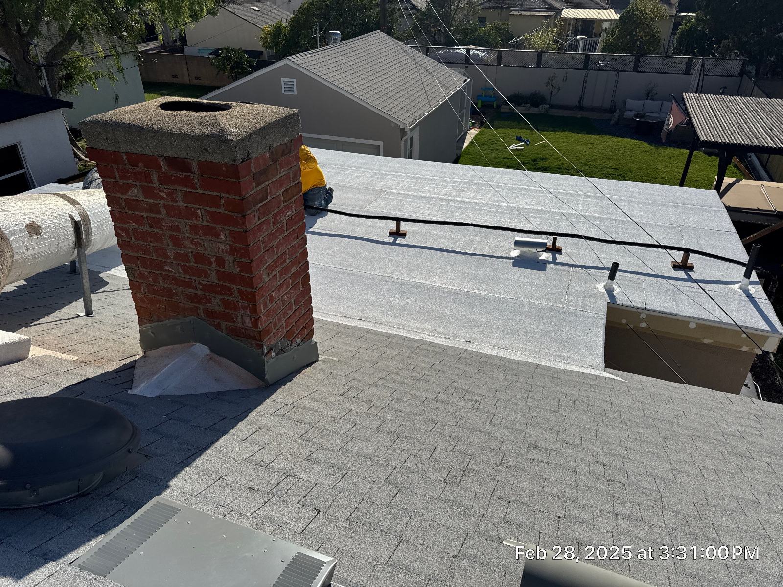 Brick chimney, new flat roof membrane, asphalt shingle slope, worker in background in Burbank | Roof Replacement Inc Brick chimney, new flat roof membrane, asphalt shingle slope, worker in background — Burbank — Roof Replacement Inc