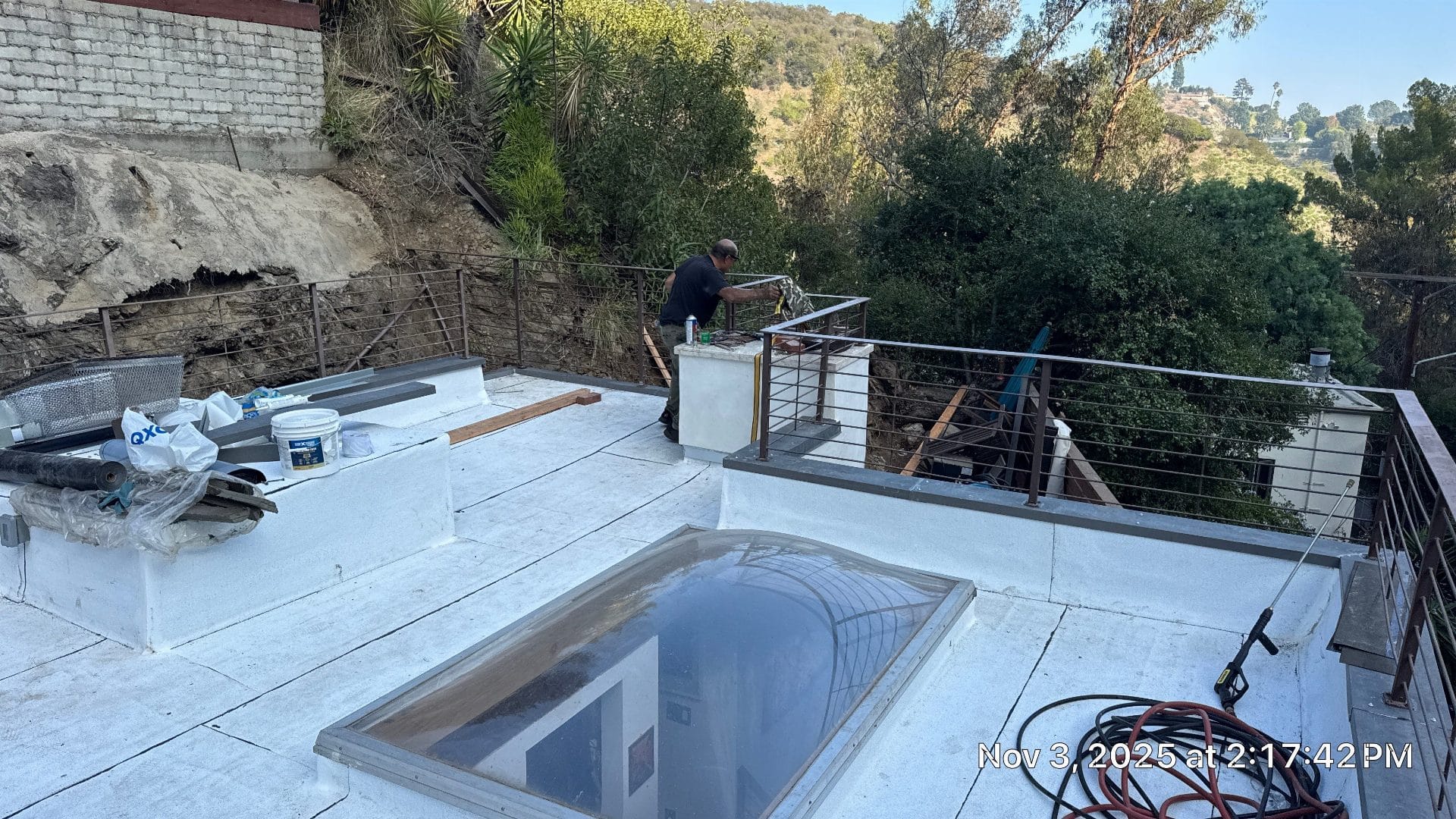 White flat roof with skylight, worker at railing, tools and buckets — Beverly Hills — Roof Replacement Inc