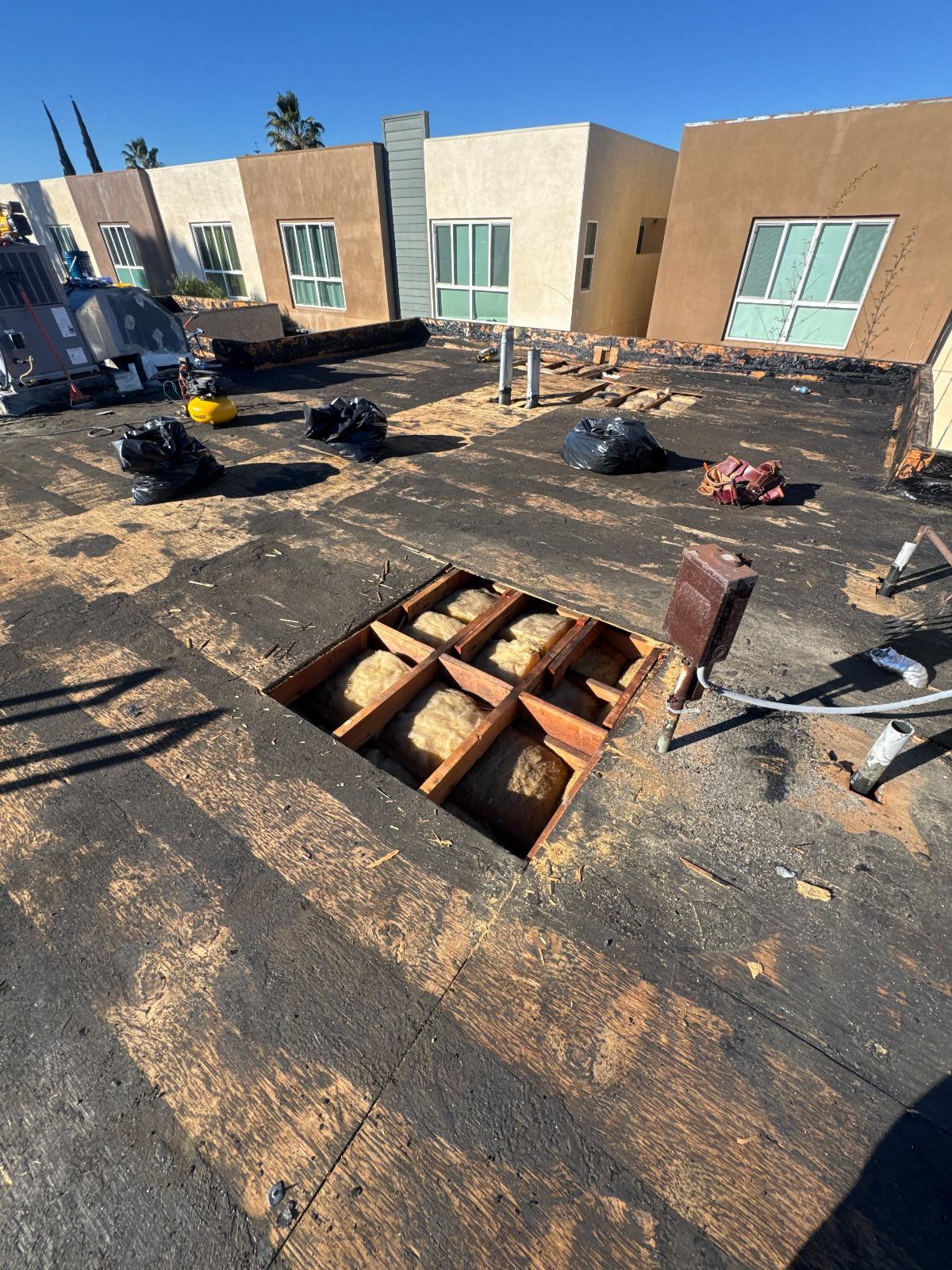 Flat roof tear-off exposing wood joists and fiberglass batt insulation below in Van Nuys | Roof Replacement Inc Flat roof tear-off exposing wood joists and fiberglass batt insulation below — Van Nuys — Roof Replacement Inc