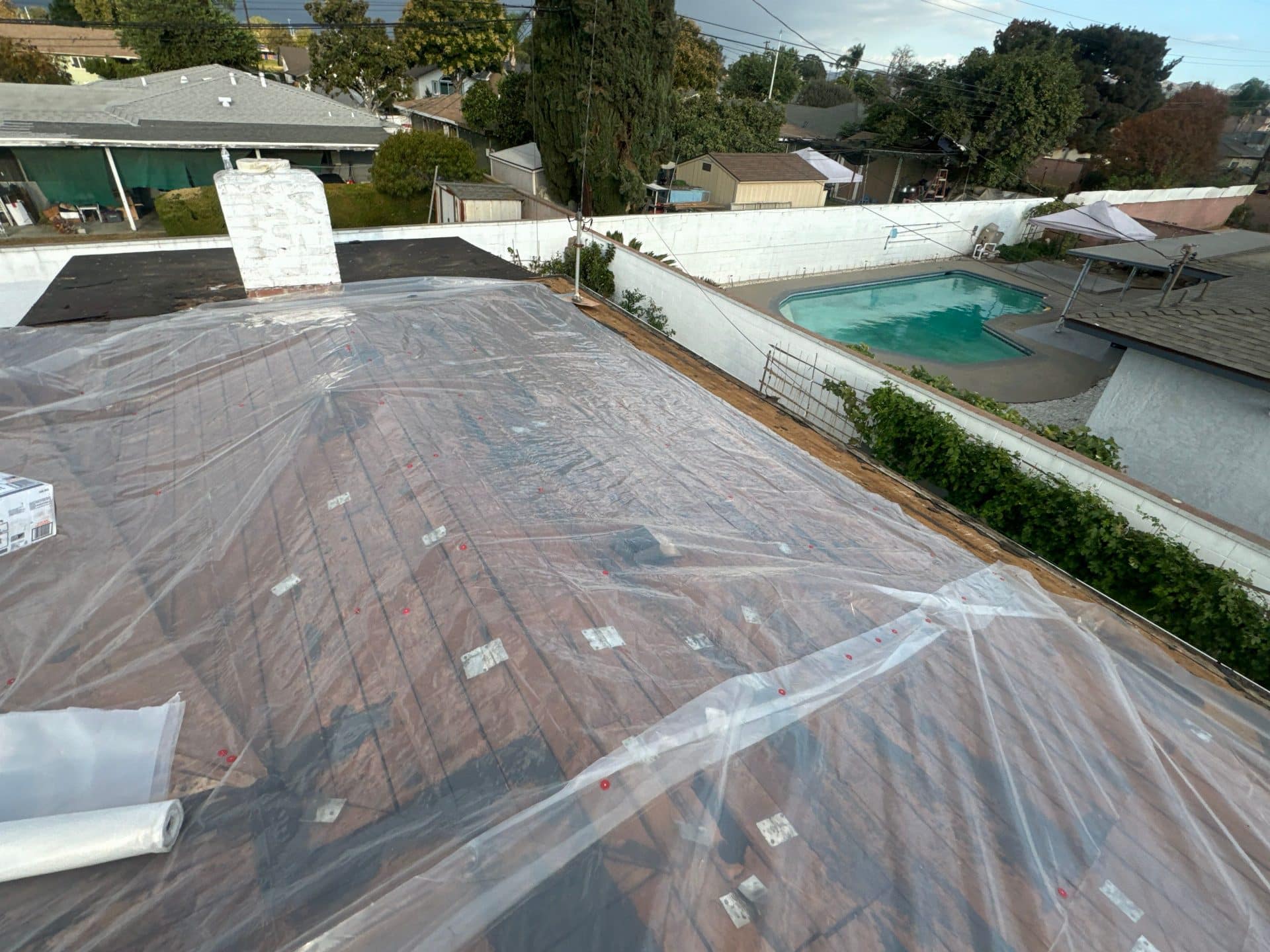 Flat roof deck covered with clear plastic sheeting and fasteners, chimney visible | Roof Replacement Inc Flat roof deck covered with clear plastic sheeting and fasteners, chimney visible — Roof Replacement Inc