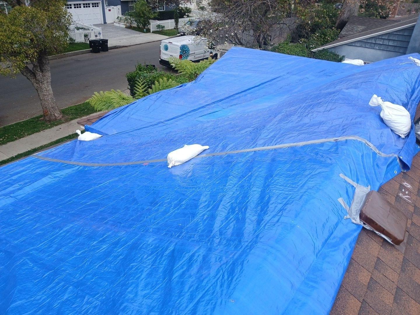 Blue polyethylene tarp weighted with sandbags covering residential roof before tear-off, Los Angeles County